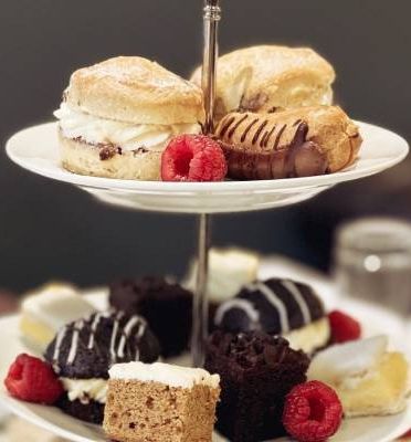 Two-tiered cake stand with assorted pastries, cakes, and fresh raspberries