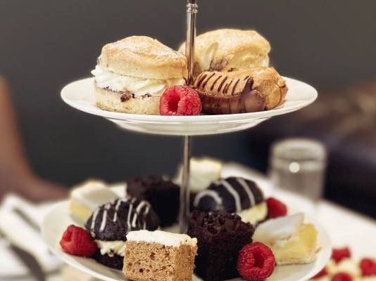 Two-tiered cake stand with assorted pastries, cakes, and fresh raspberries