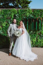 Bride and groom posing together outdoors in front of a green leafy backdrop with wedding attire