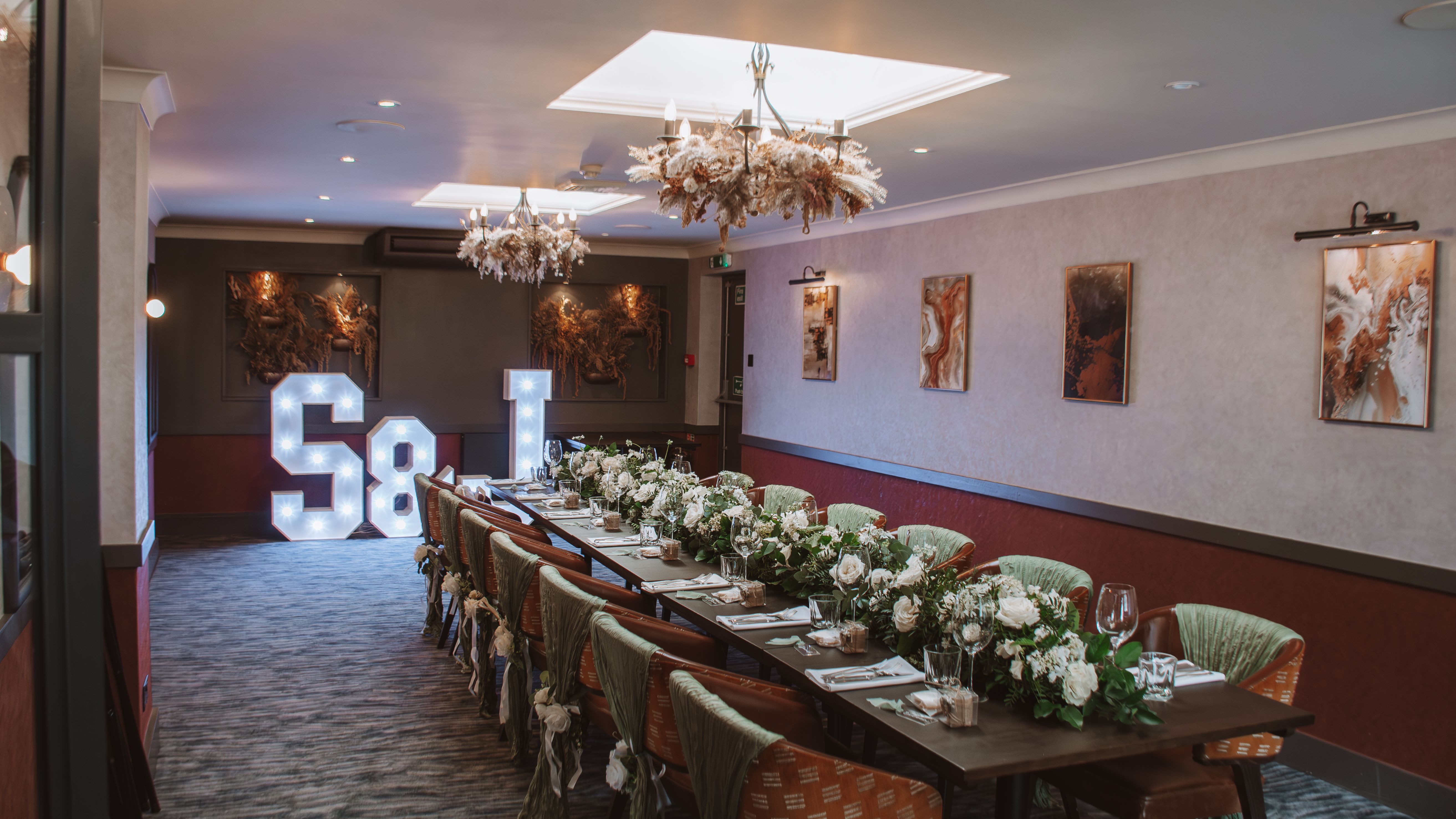 Elegant banquet table with floral arrangements, decorated chairs, and light-up S & J letters at the end of the room.