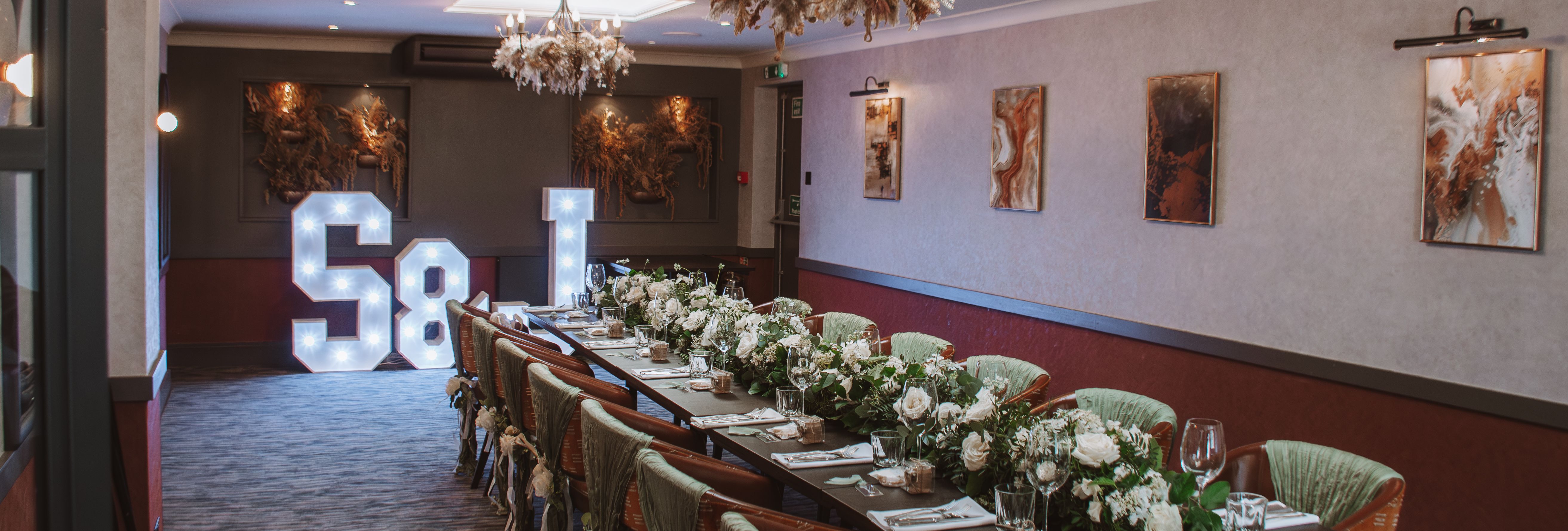 Elegant banquet table with floral arrangements, decorated chairs, and light-up S & J letters at the end of the room.