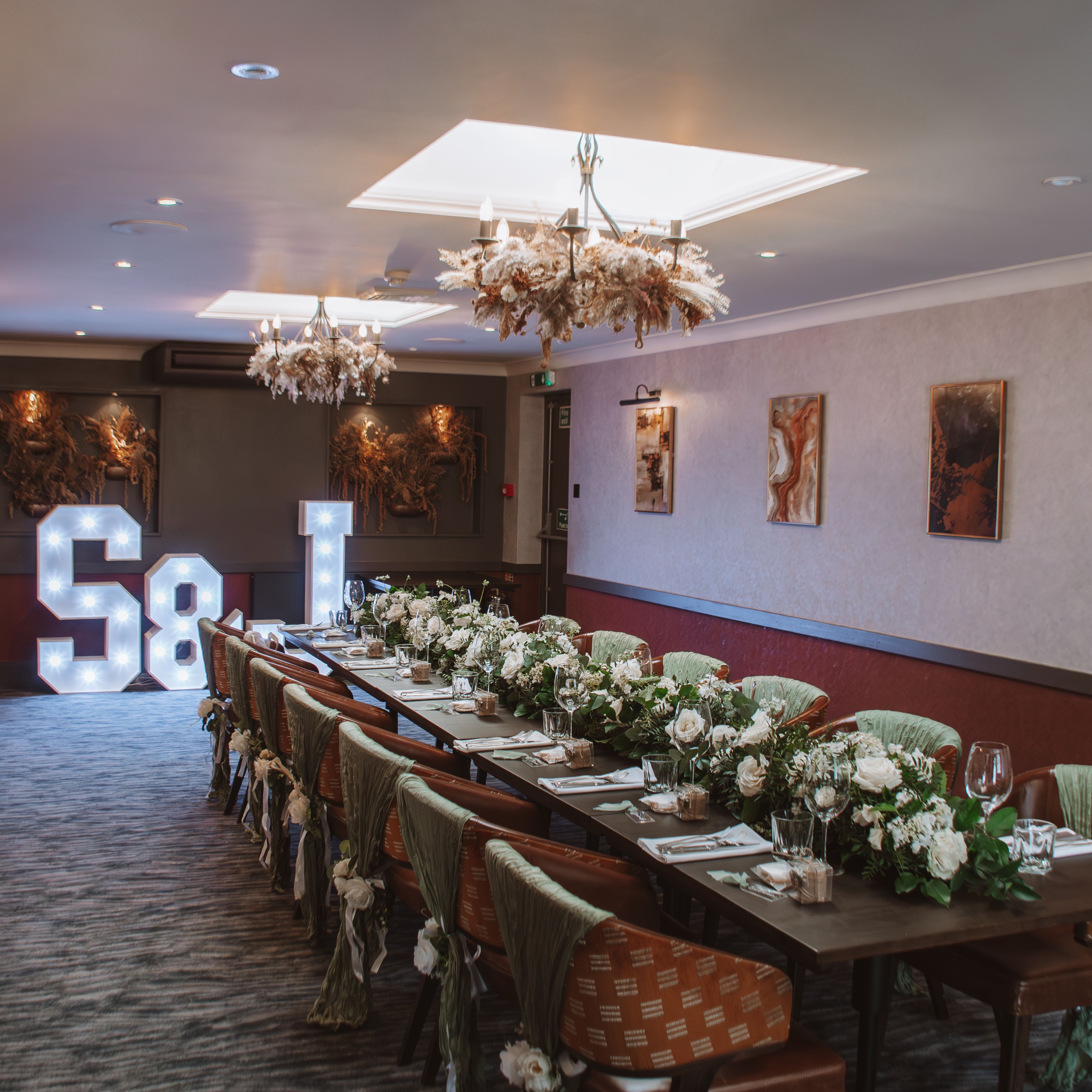 Elegant banquet table with floral arrangements, decorated chairs, and light-up S & J letters at the end of the room.