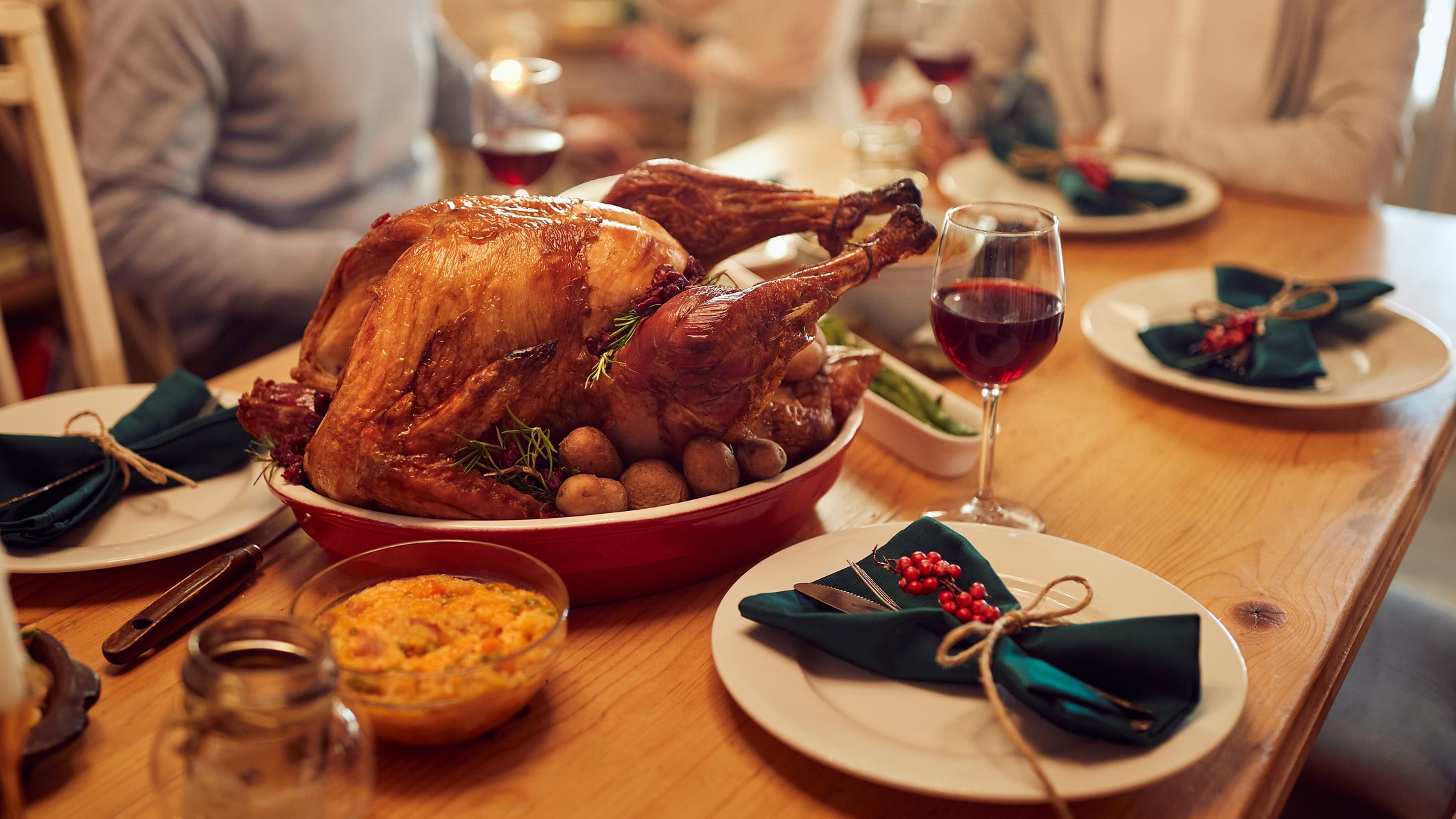 Festive dinner table set with a roasted turkey, red wine, and holiday-themed place settings, surrounded by family members ready to enjoy a holiday meal together.