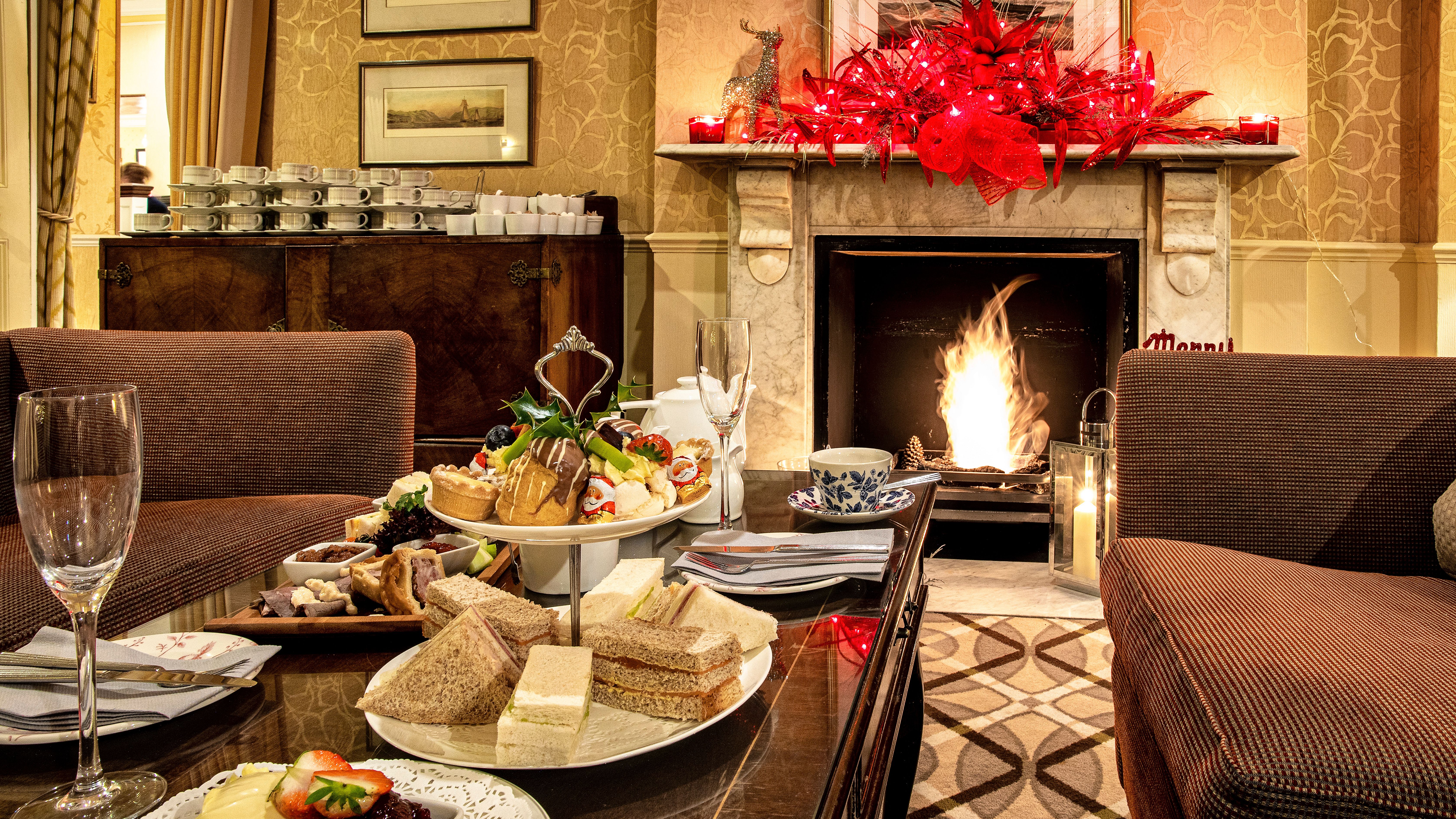 Festive afternoon tea set up in a cozy living room with a fireplace and red holiday decorations