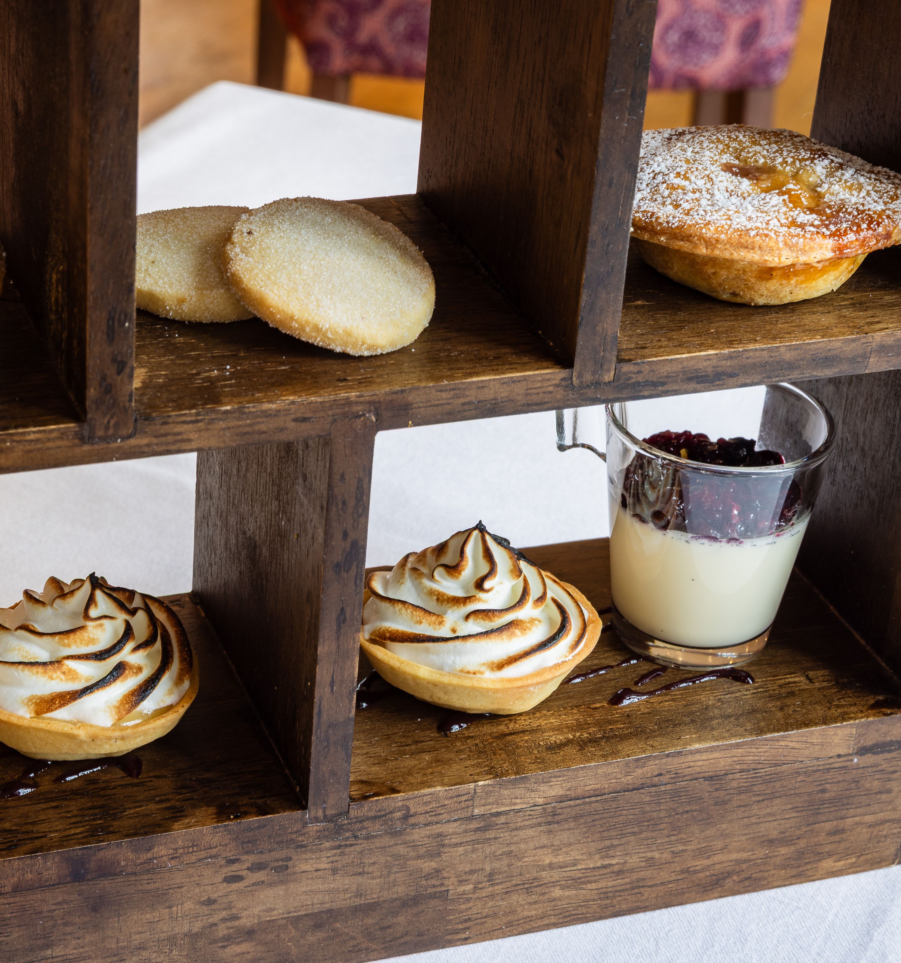 Afternoon tea on a wooden shelf with shortbread, pastries and lemon meringue pies