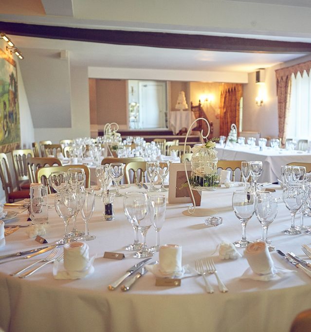 A round table elegantly set for a formal event, covered with a white tablecloth and surrounded by gold chairs.