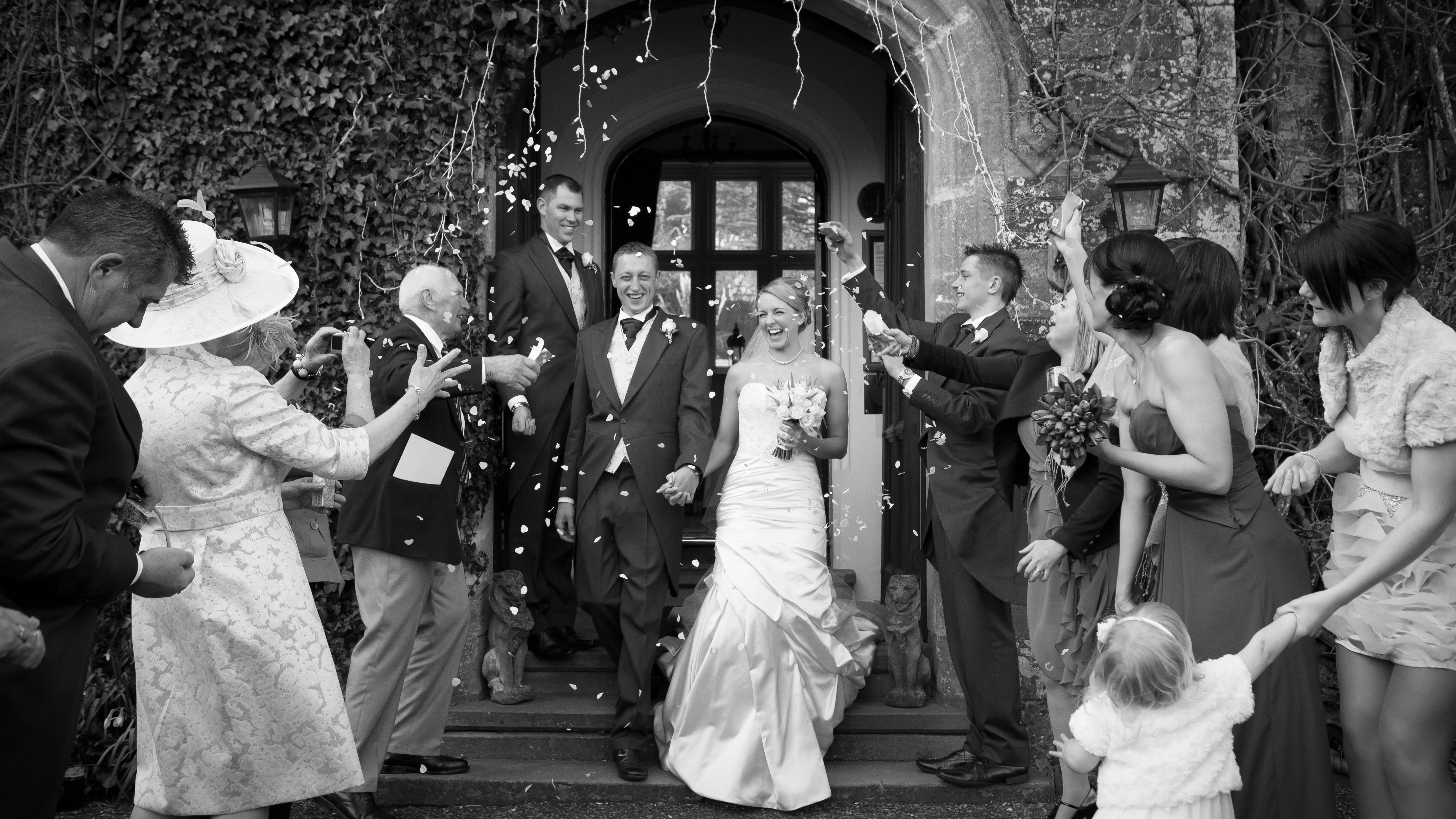 A joyful bride and groom exit a stone doorway as guests shower them with confetti.