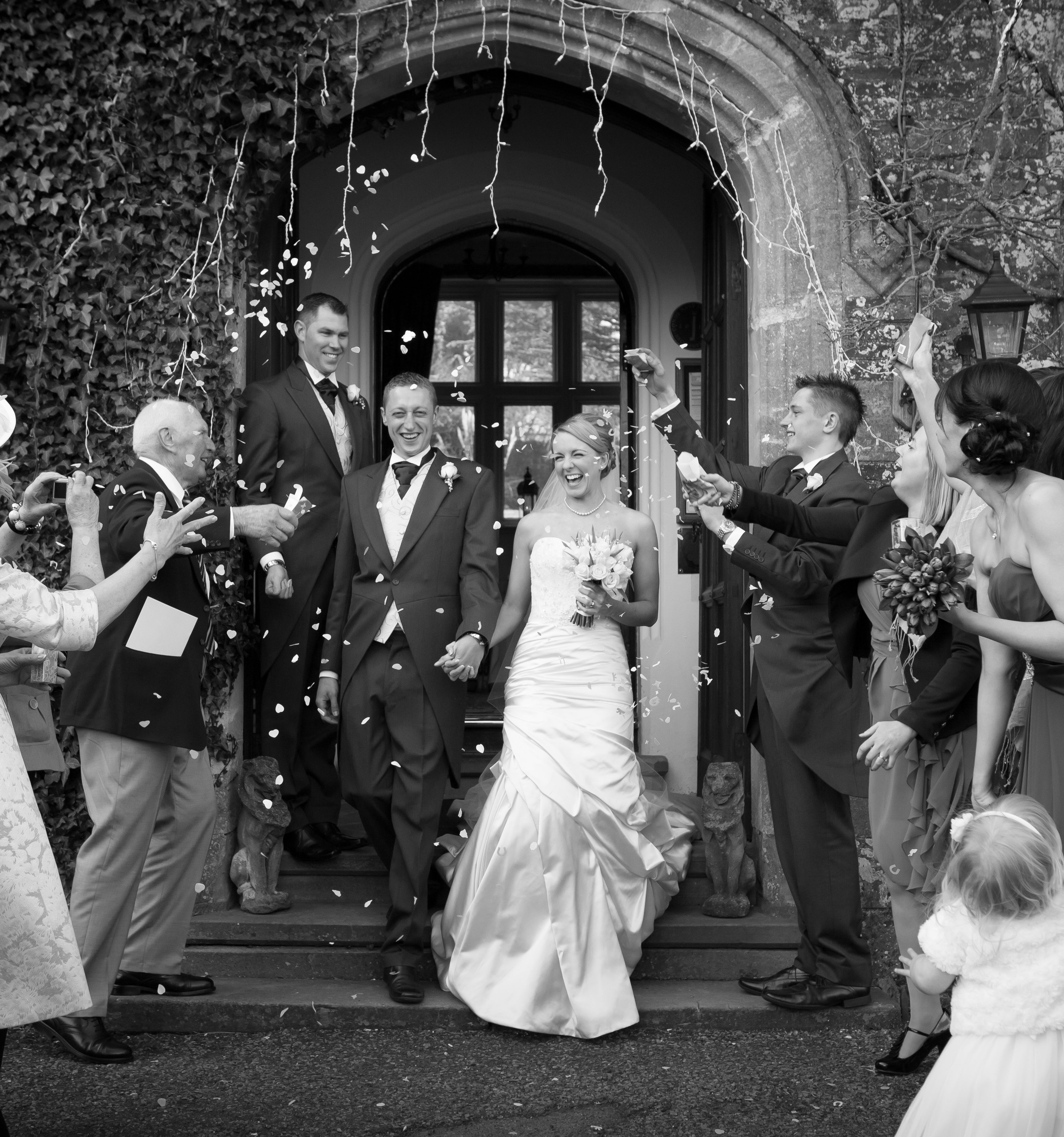 A joyful bride and groom exit a stone doorway as guests shower them with confetti.