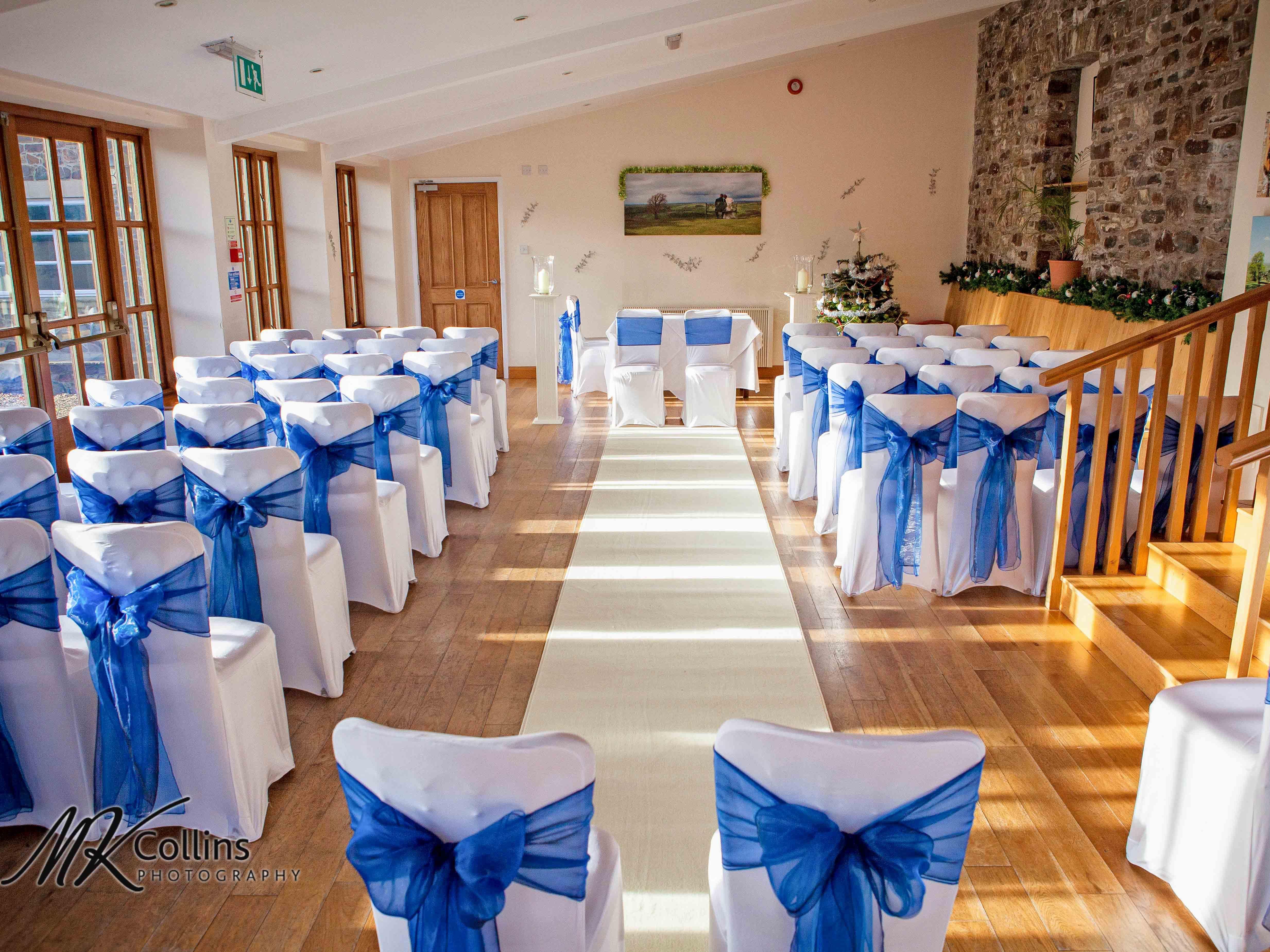 A beautifully decorated wedding ceremony room with rows of white chairs adorned with blue organza sashes tied into bows.