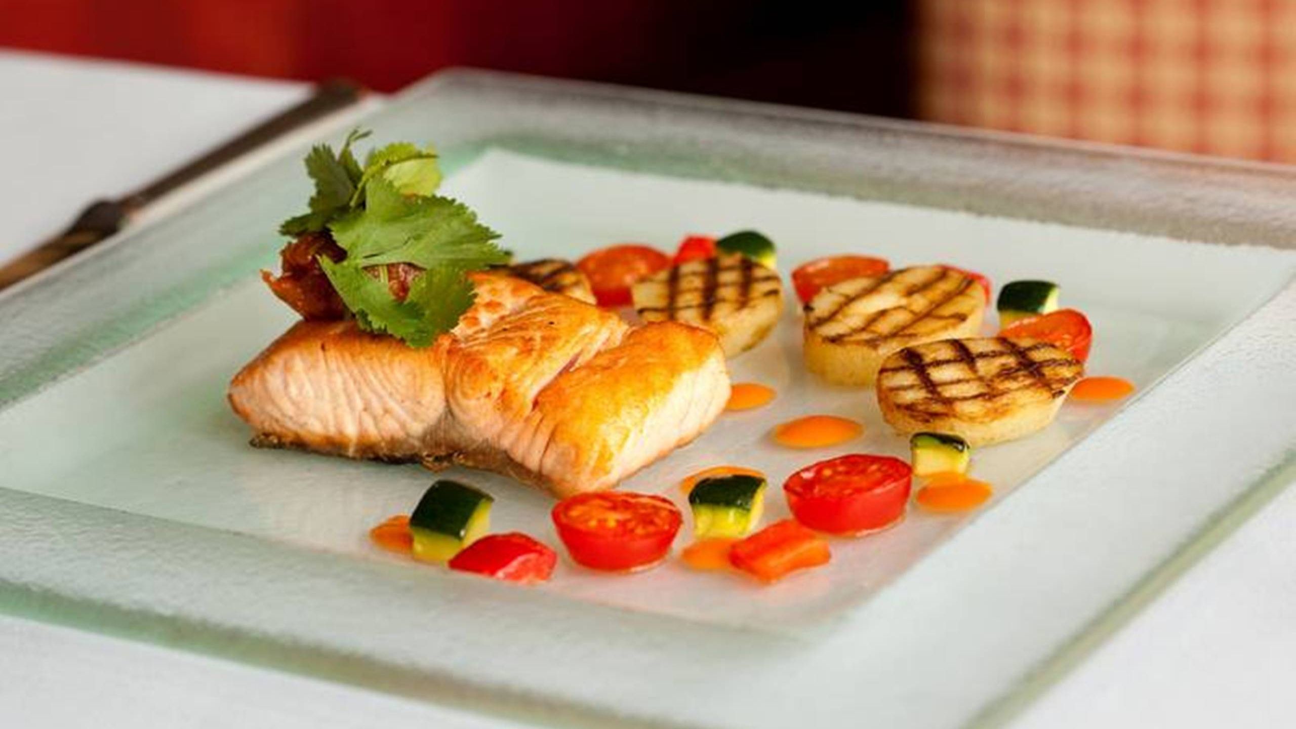 A gourmet dish featuring a seared salmon fillet with a golden-brown crust, garnished with fresh herbs and crispy bacon.