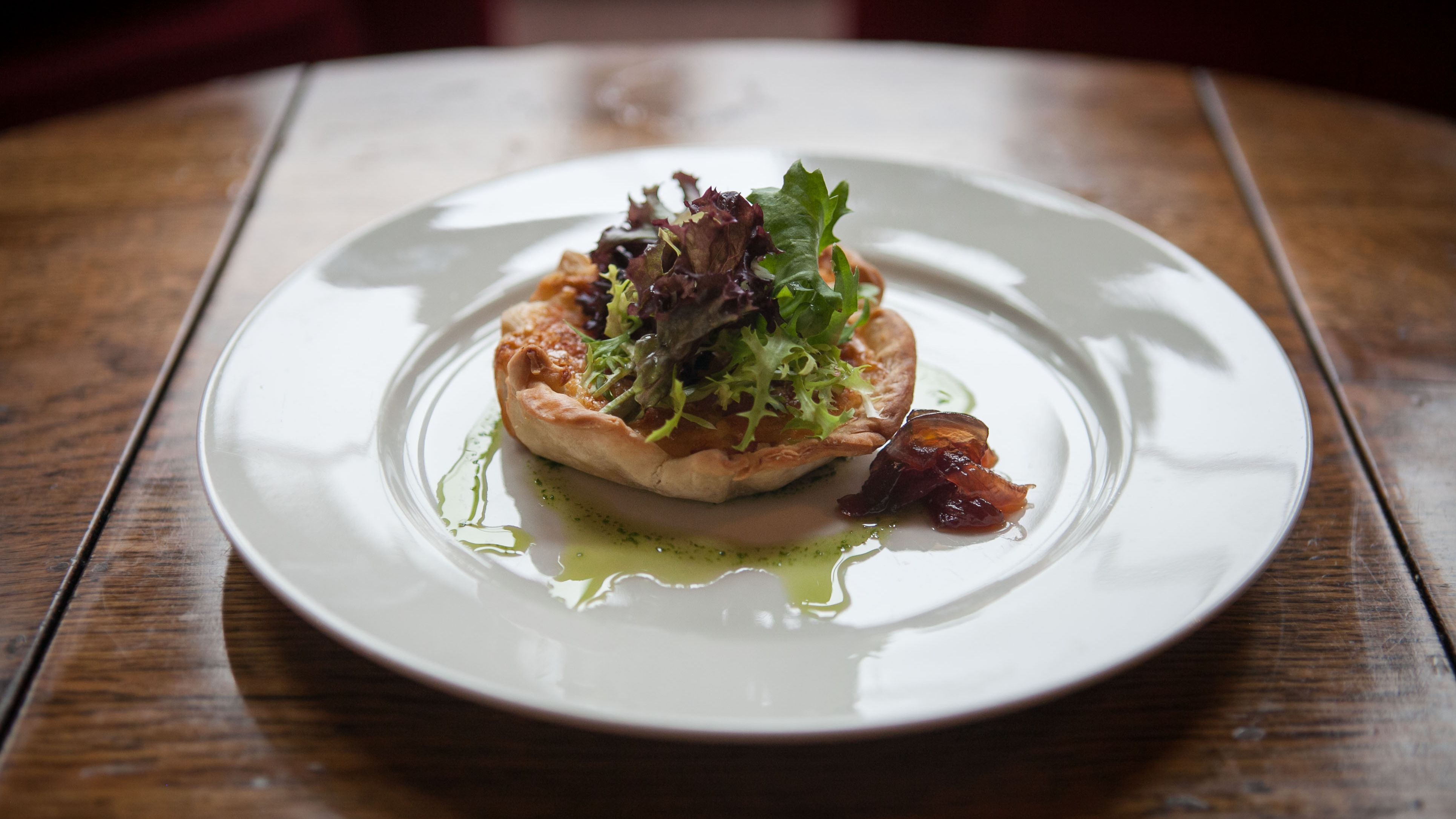 A savory tart with a golden, flaky crust, topped with fresh mixed greens and served with a side of caramelized onions
