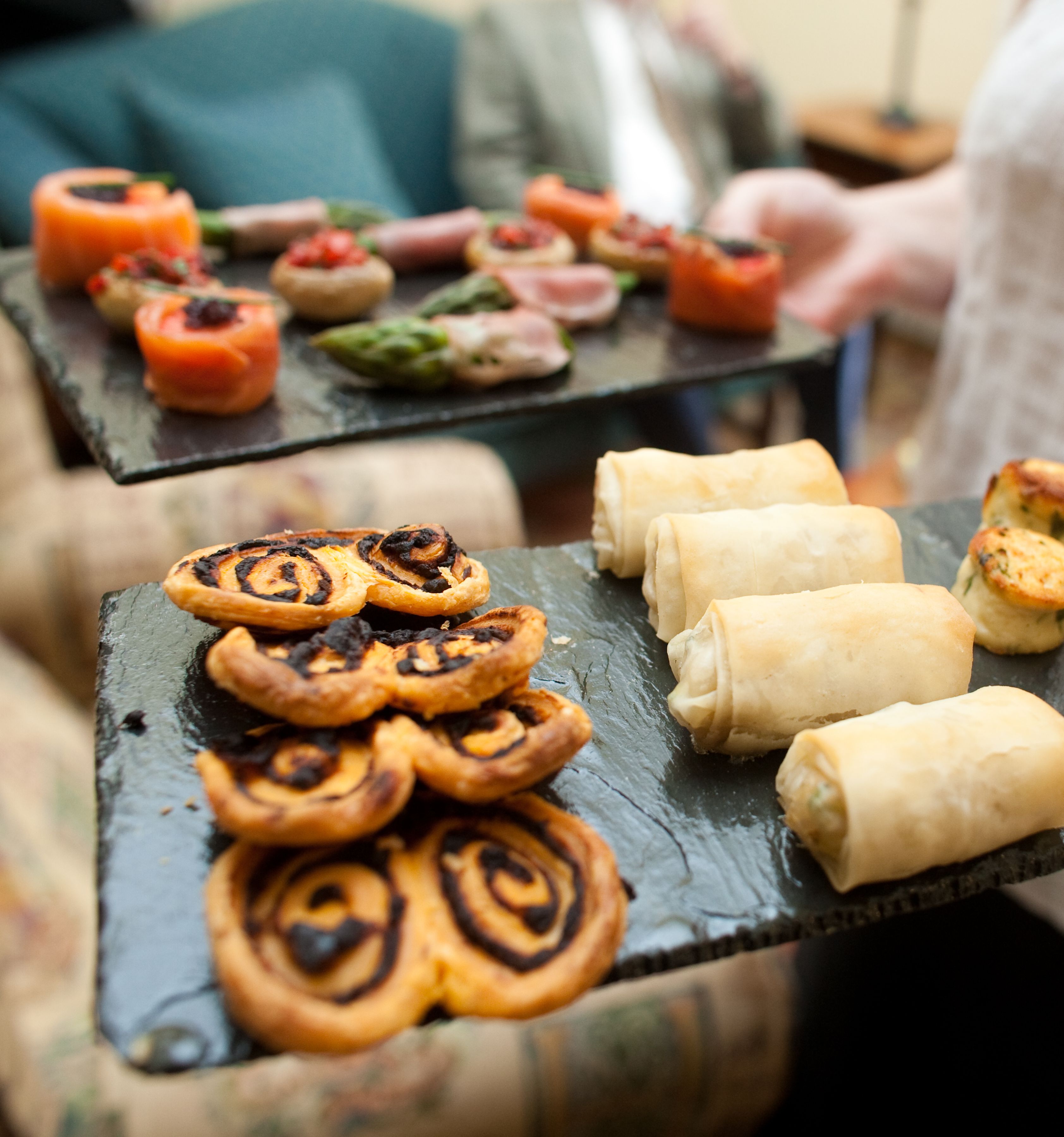 Two trays of assorted appetizers being served at a gathering, including puff pastry pinwheels