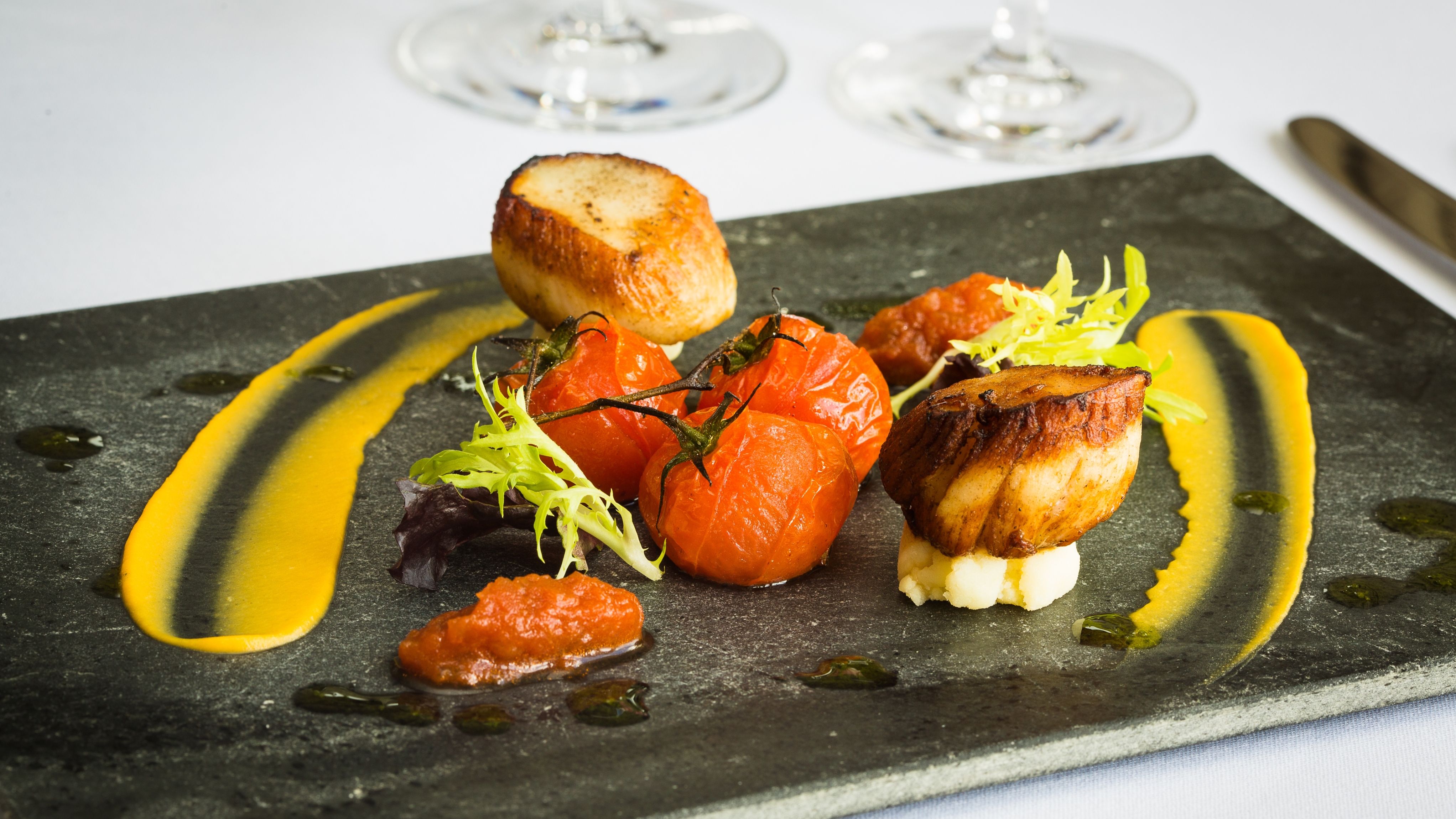 A gourmet dish presented on a dark slate plate, featuring seared scallops on a bed of mashed potatoes