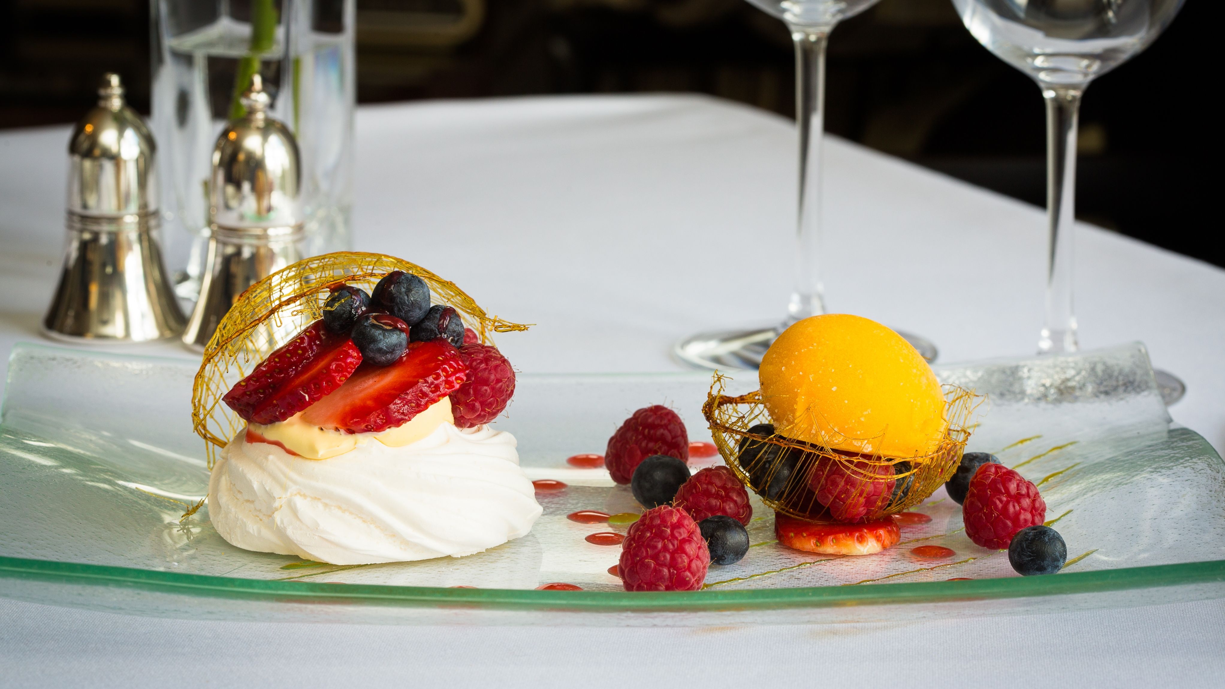 A plated dessert featuring a pavlova topped with fresh strawberries, raspberries, and blueberries