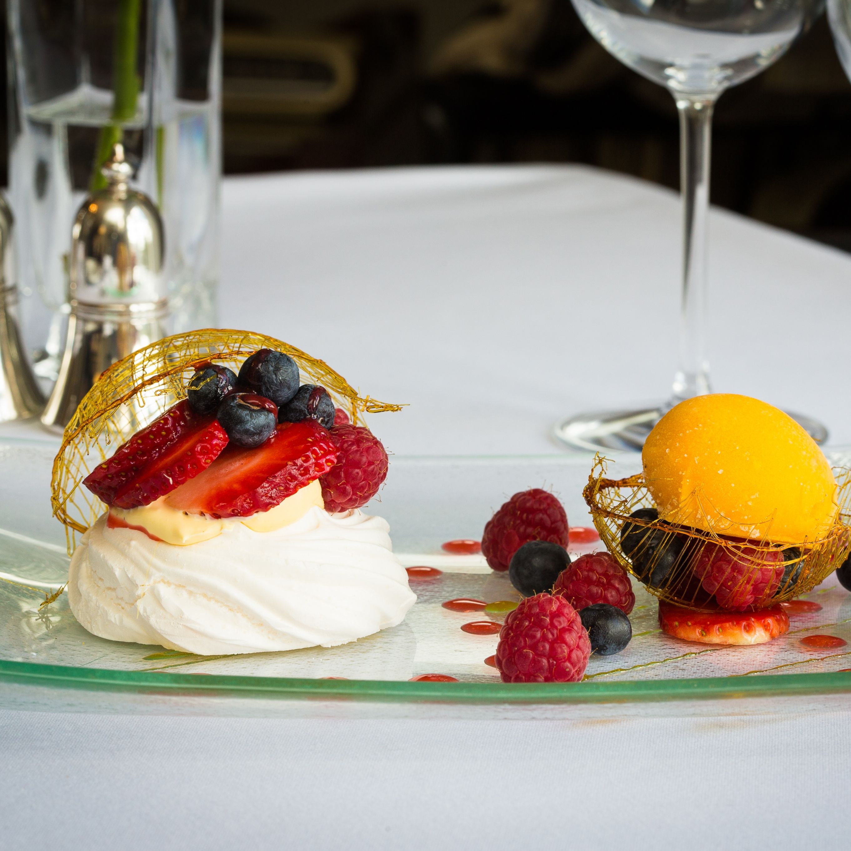A plated dessert featuring a pavlova topped with fresh strawberries, raspberries, and blueberries