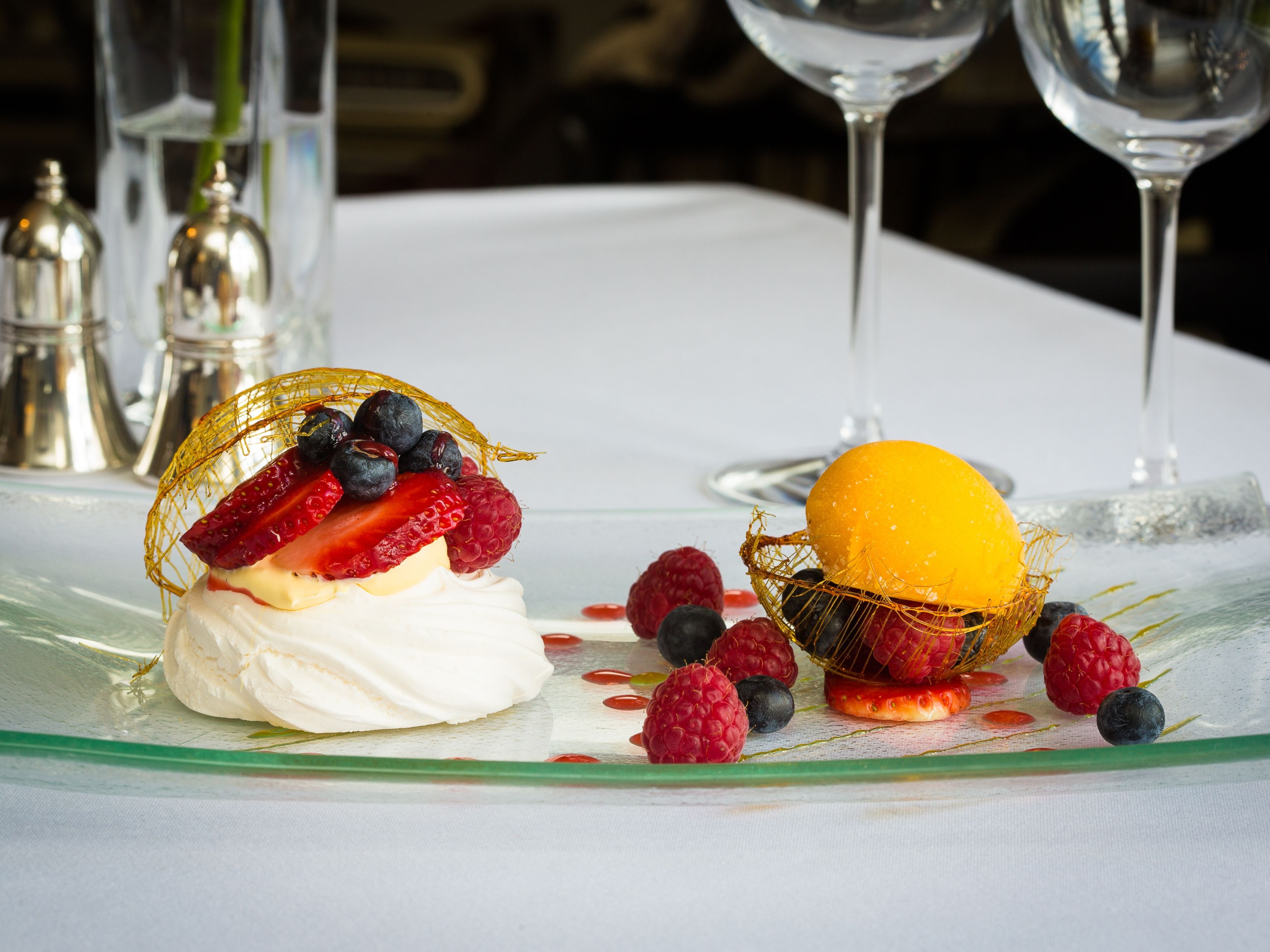 A plated dessert featuring a pavlova topped with fresh strawberries, raspberries, and blueberries
