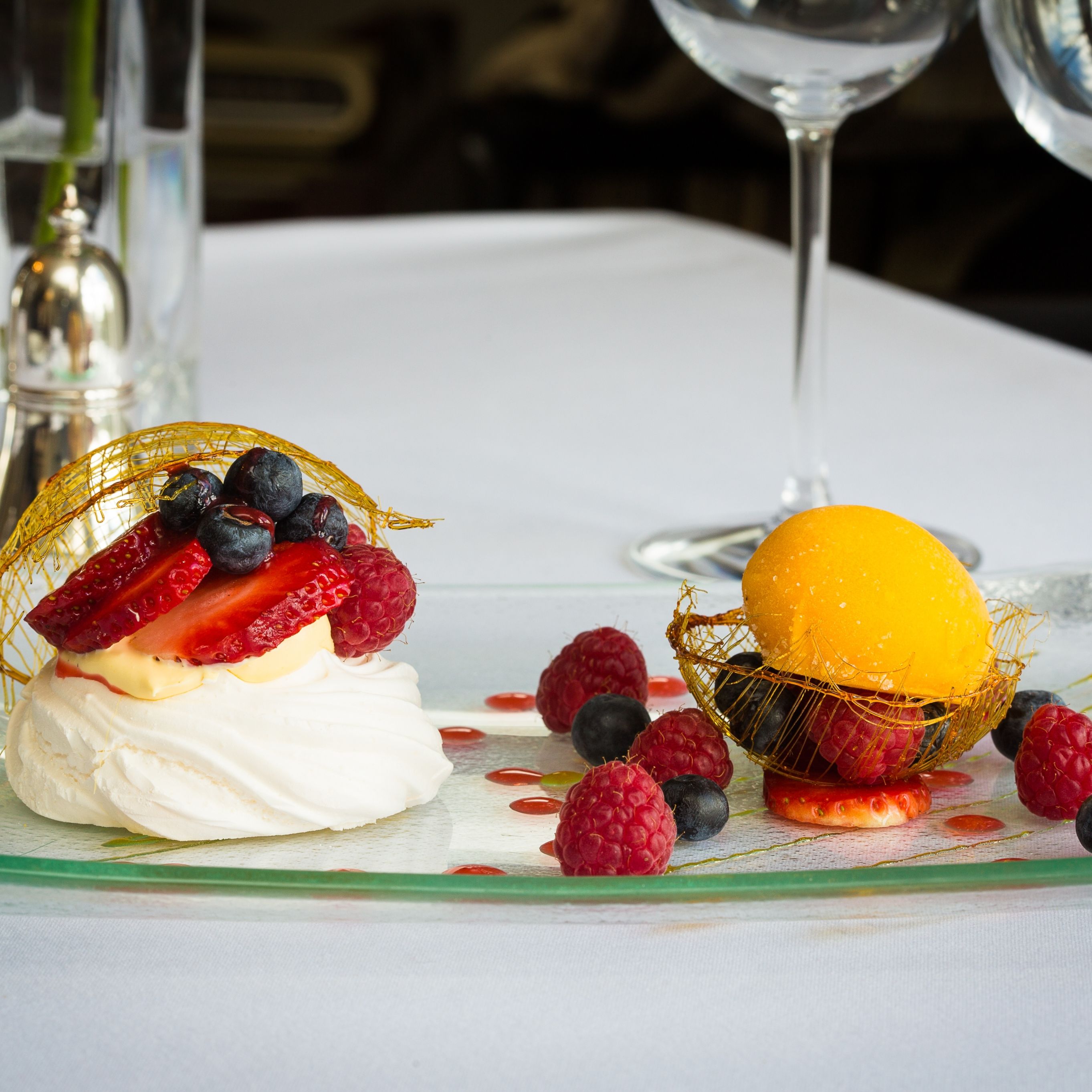 A plated dessert featuring a pavlova topped with fresh strawberries, raspberries, and blueberries