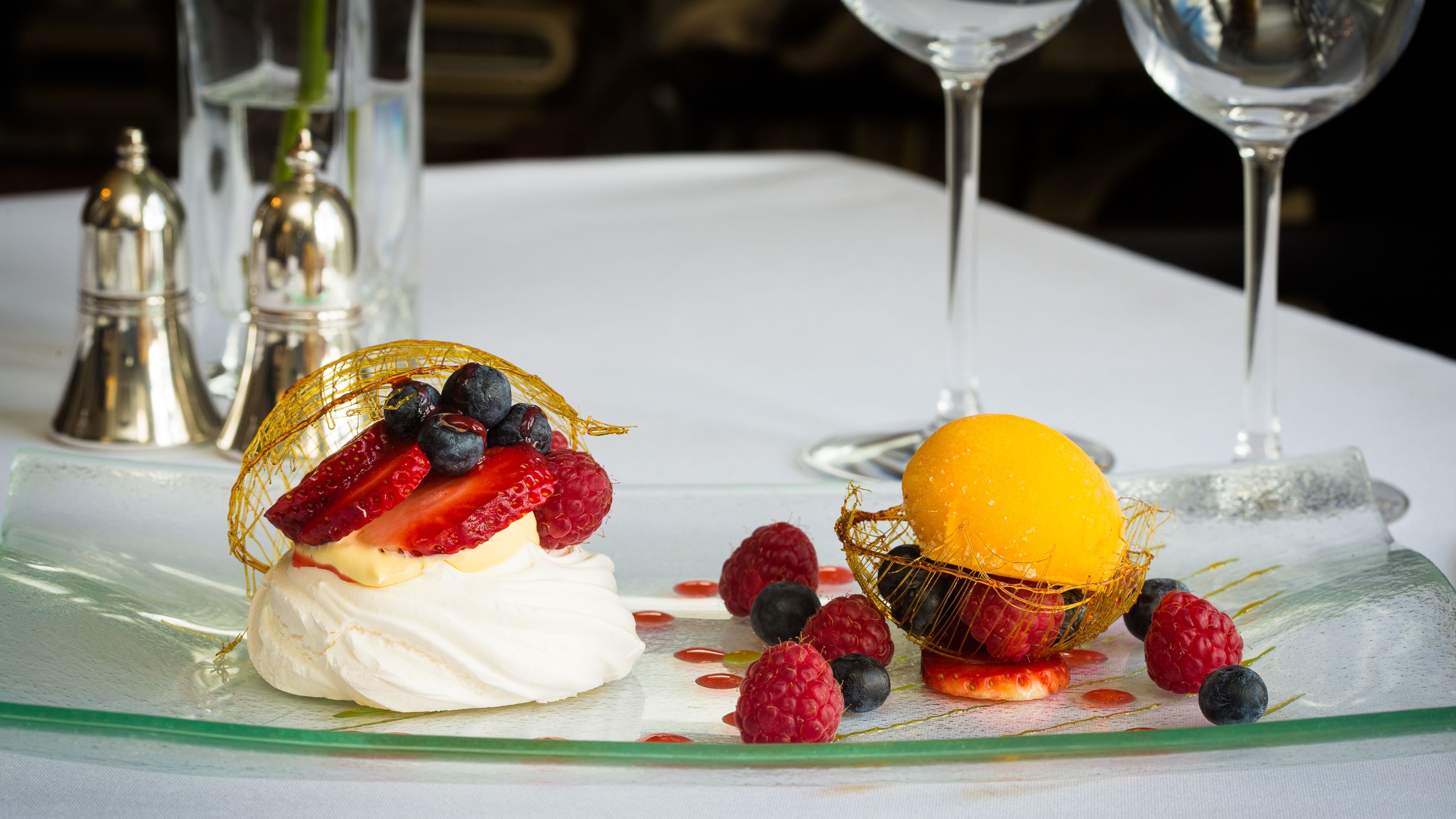 A plated dessert featuring a pavlova topped with fresh strawberries, raspberries, and blueberries