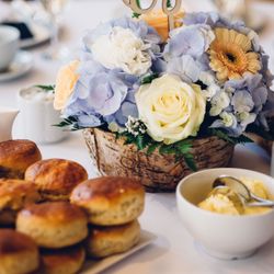 A floral centerpiece with pastel hydrangeas, roses, and carnations in a rustic basket, surrounded by plates of scones