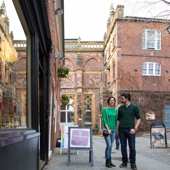 Couple walking down Gandy Street in Exeter, lined with independent shops and historic red-brick buildings