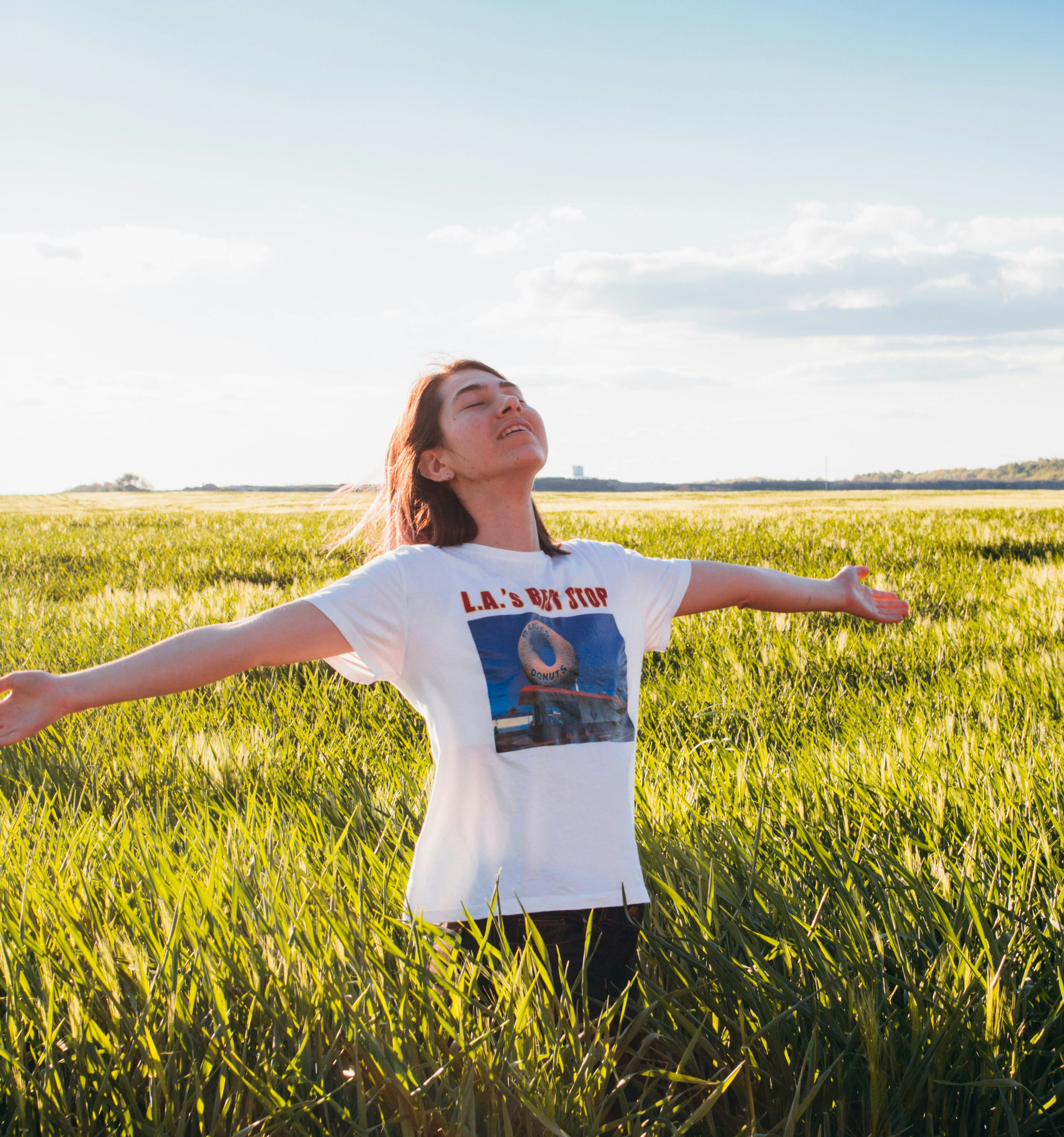 Person standing in a green field with arms outstretched under a blue sky