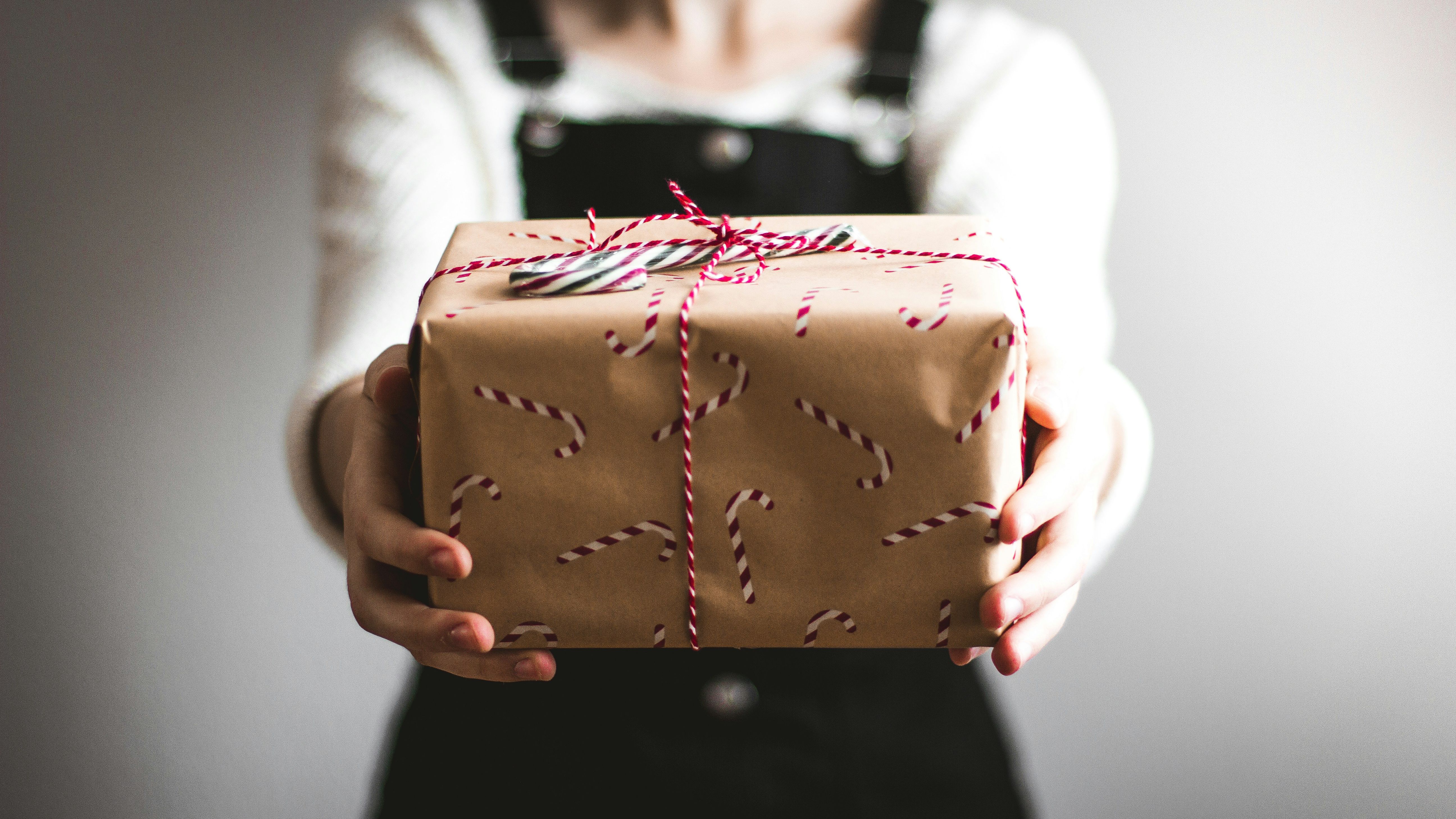 Person holding a wrapped gift with candy cane-patterned paper and red and white string
