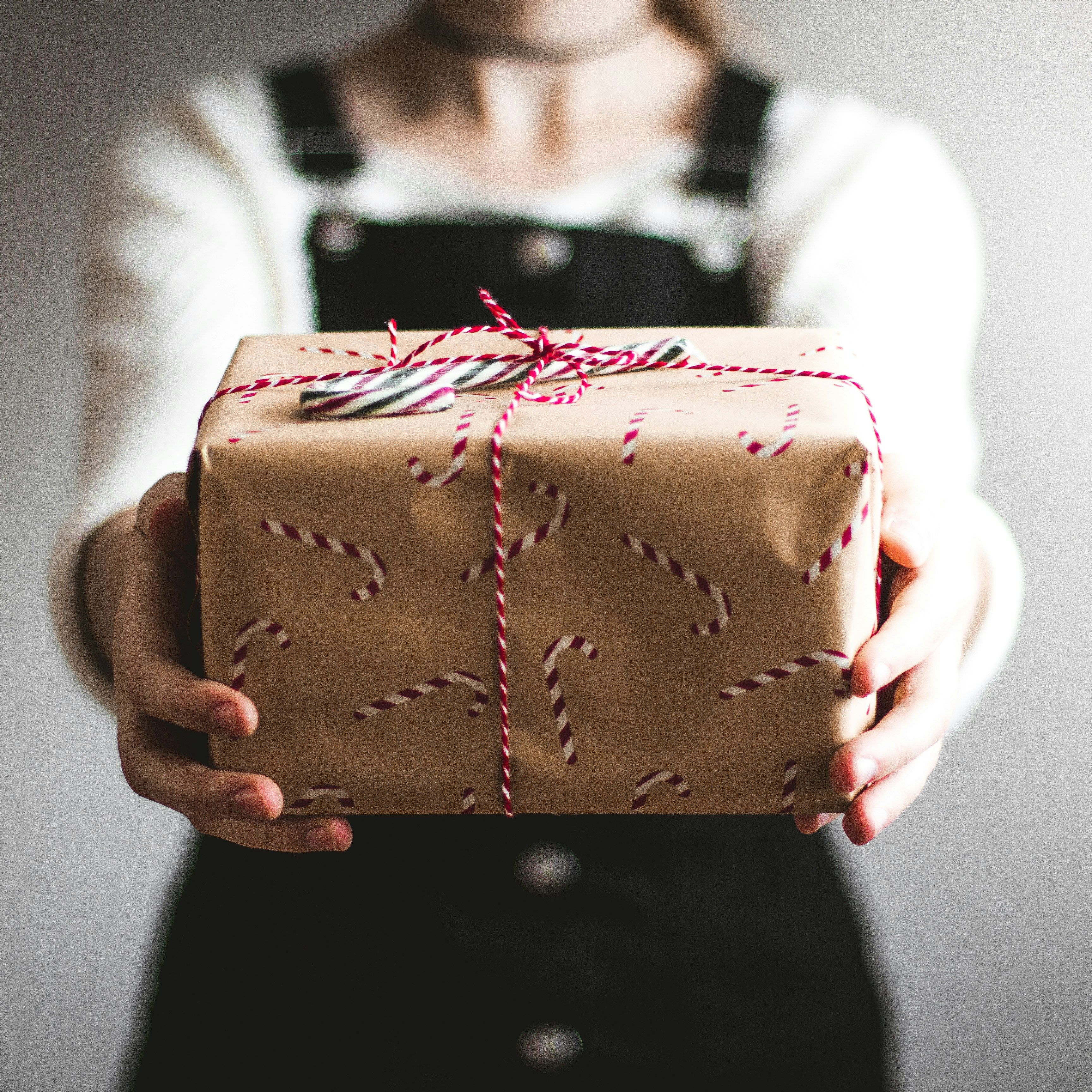 Person holding a wrapped gift with candy cane-patterned paper and red and white string