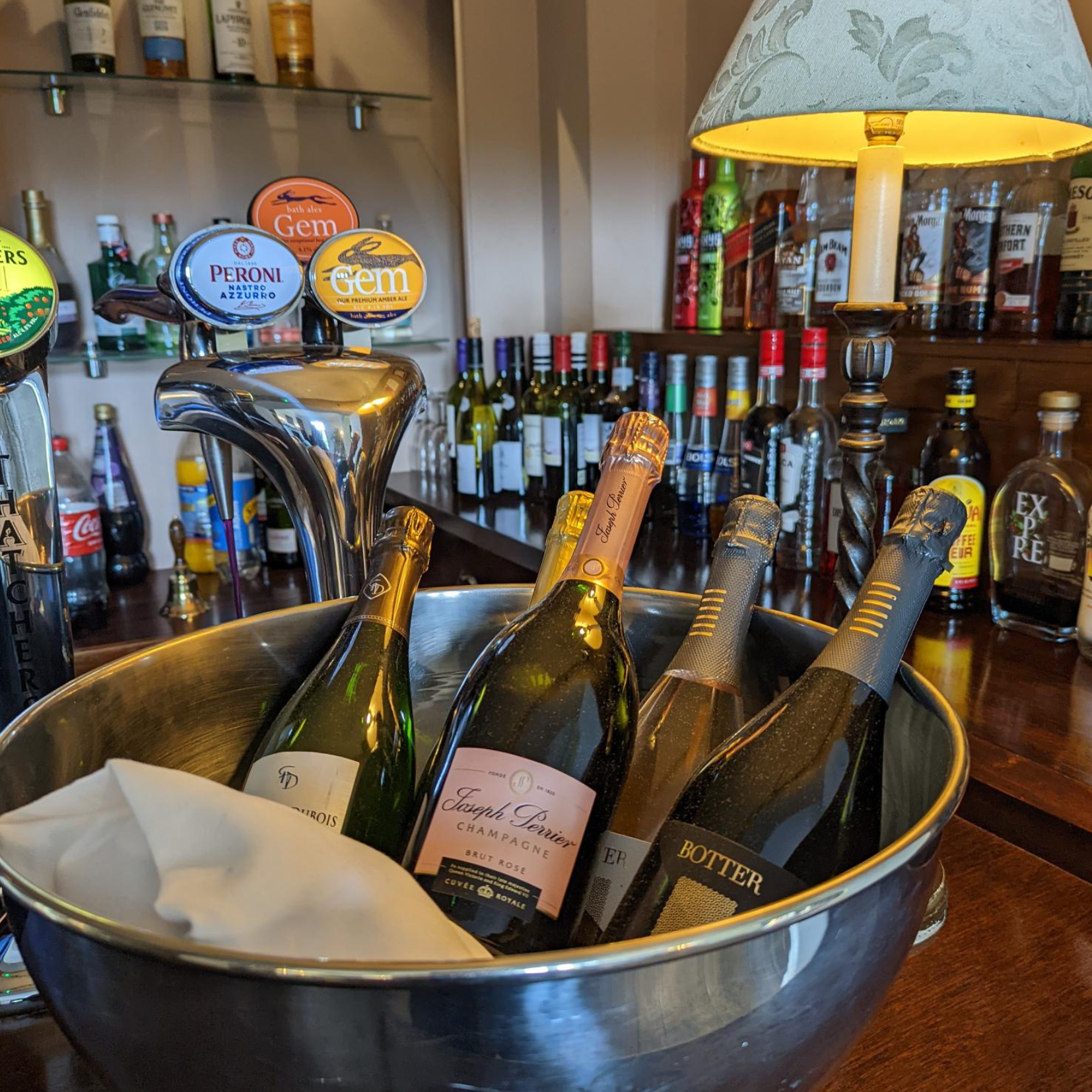 A selection of champagne and wine bottles chilling in an ice bucket on a bar counter, surrounded by beer taps and various liquor bottles.