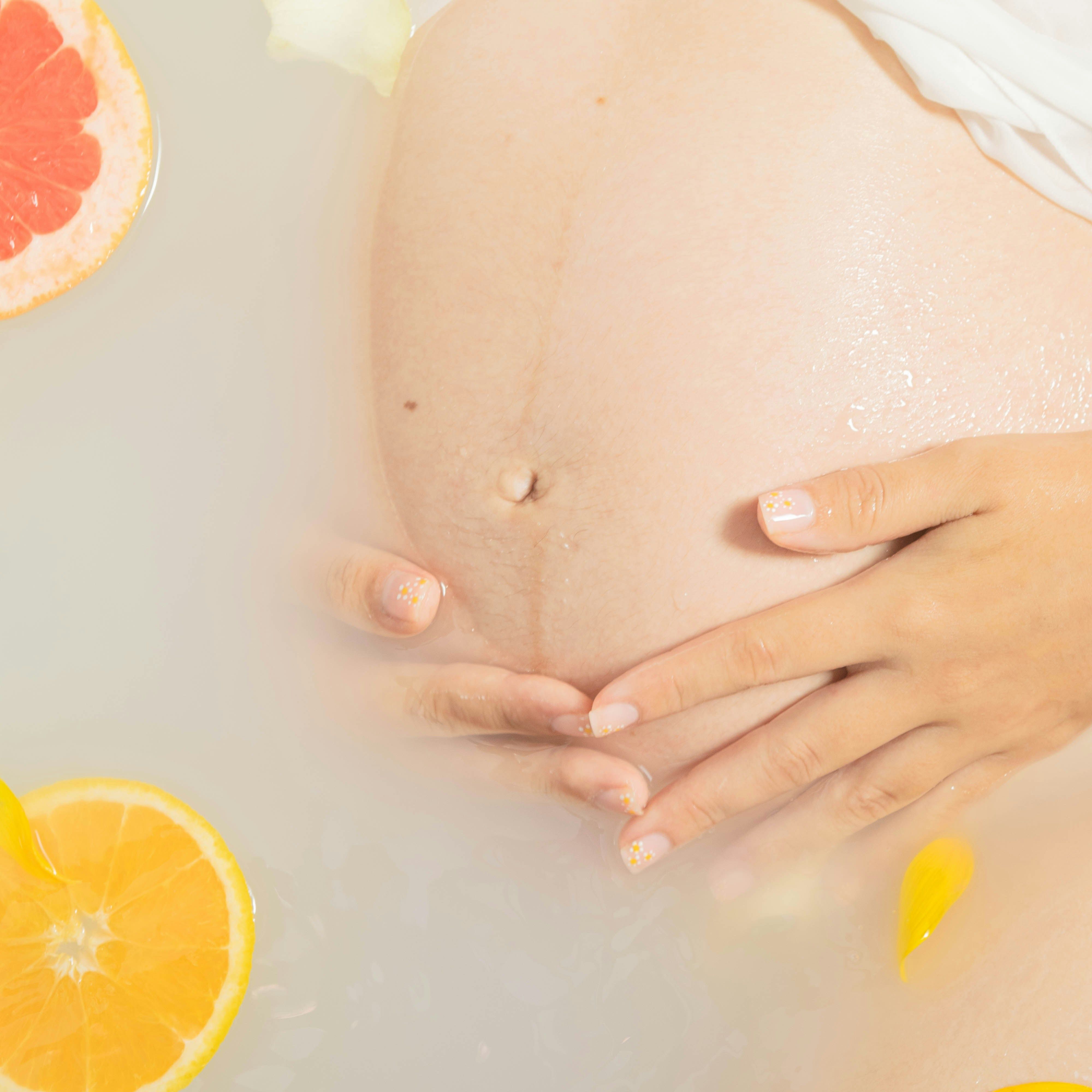 Pregnant belly in a milky bath with citrus slices and flower petals