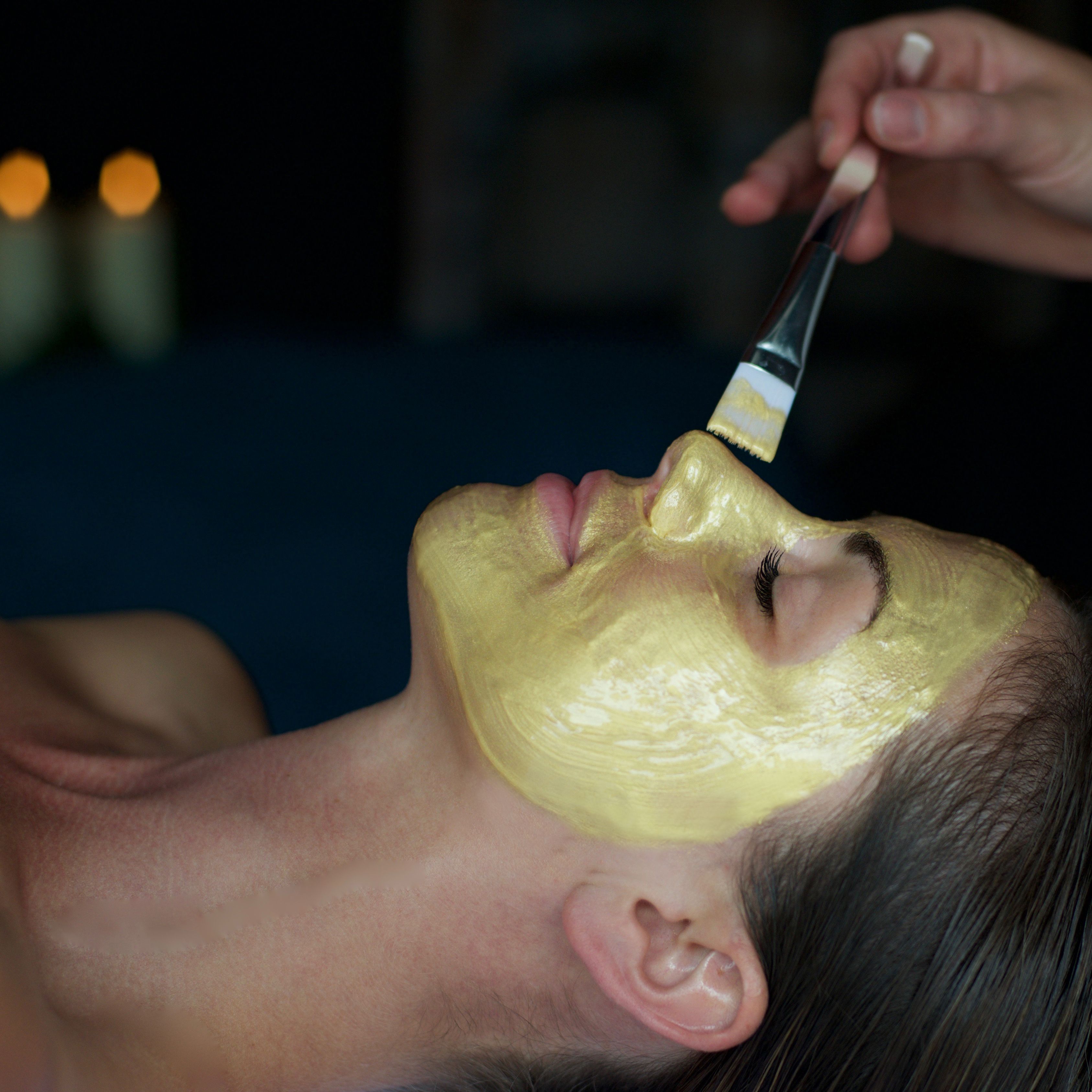 Person receiving a gold facial mask applied with a brush in a spa setting