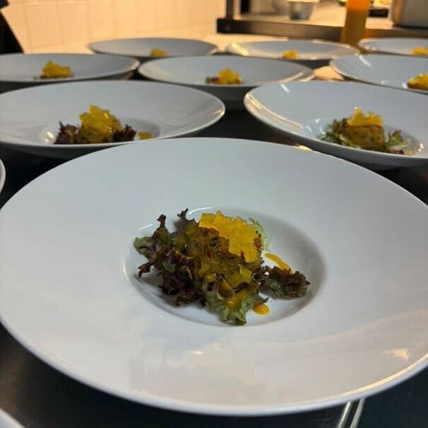 Several plates prepared with salad greens and a yellow garnish in a professional kitchen.
