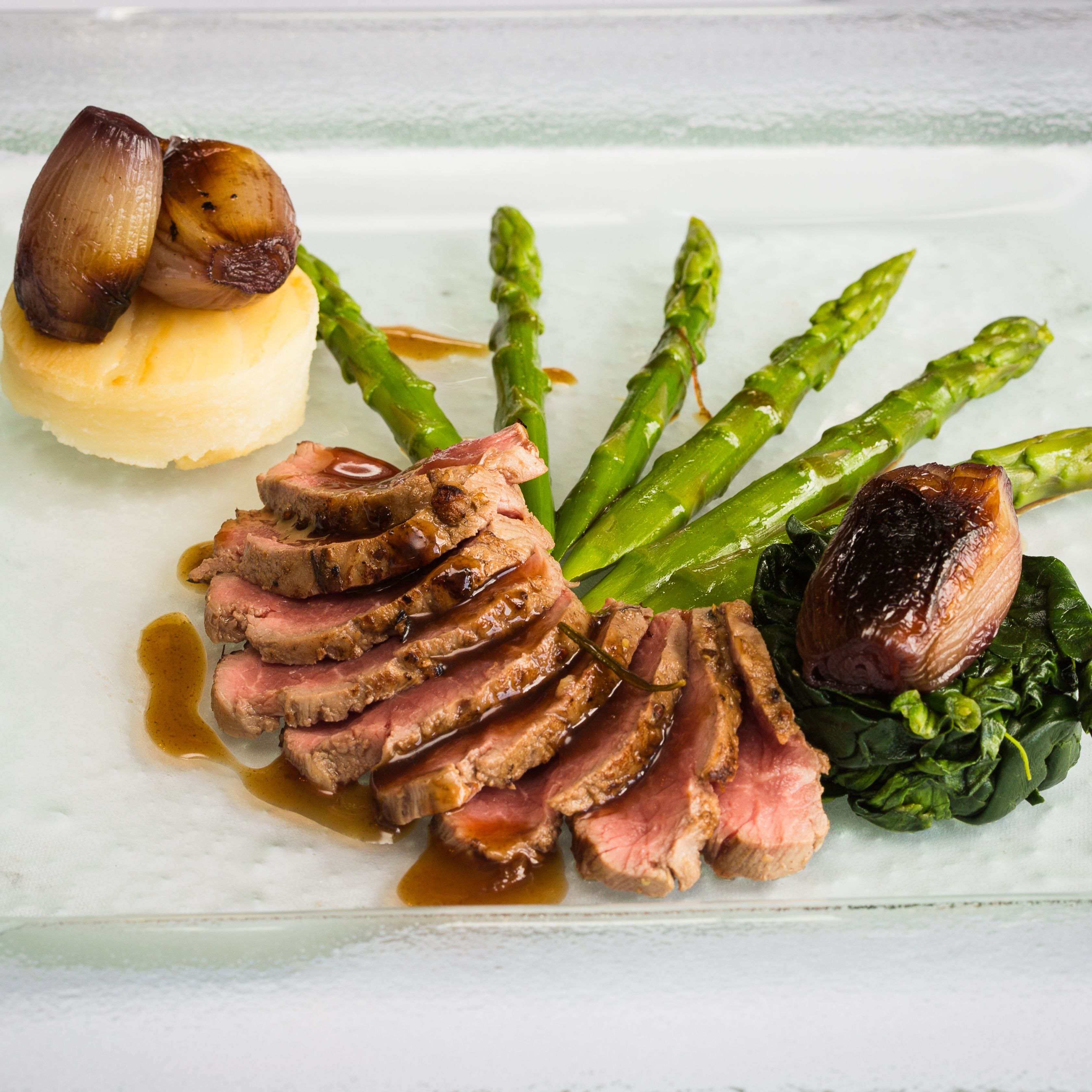 Gourmet plated dish with sliced beef, mashed potatoes, caramelized shallots, asparagus, and spinach