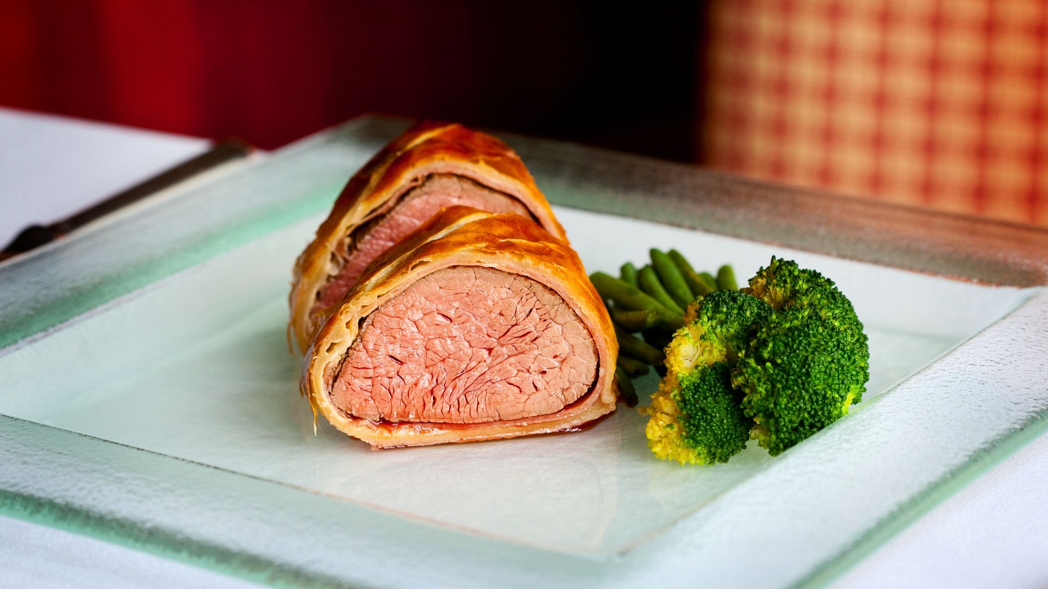 Beef Wellington slices served with green beans and broccoli on a glass plate.
