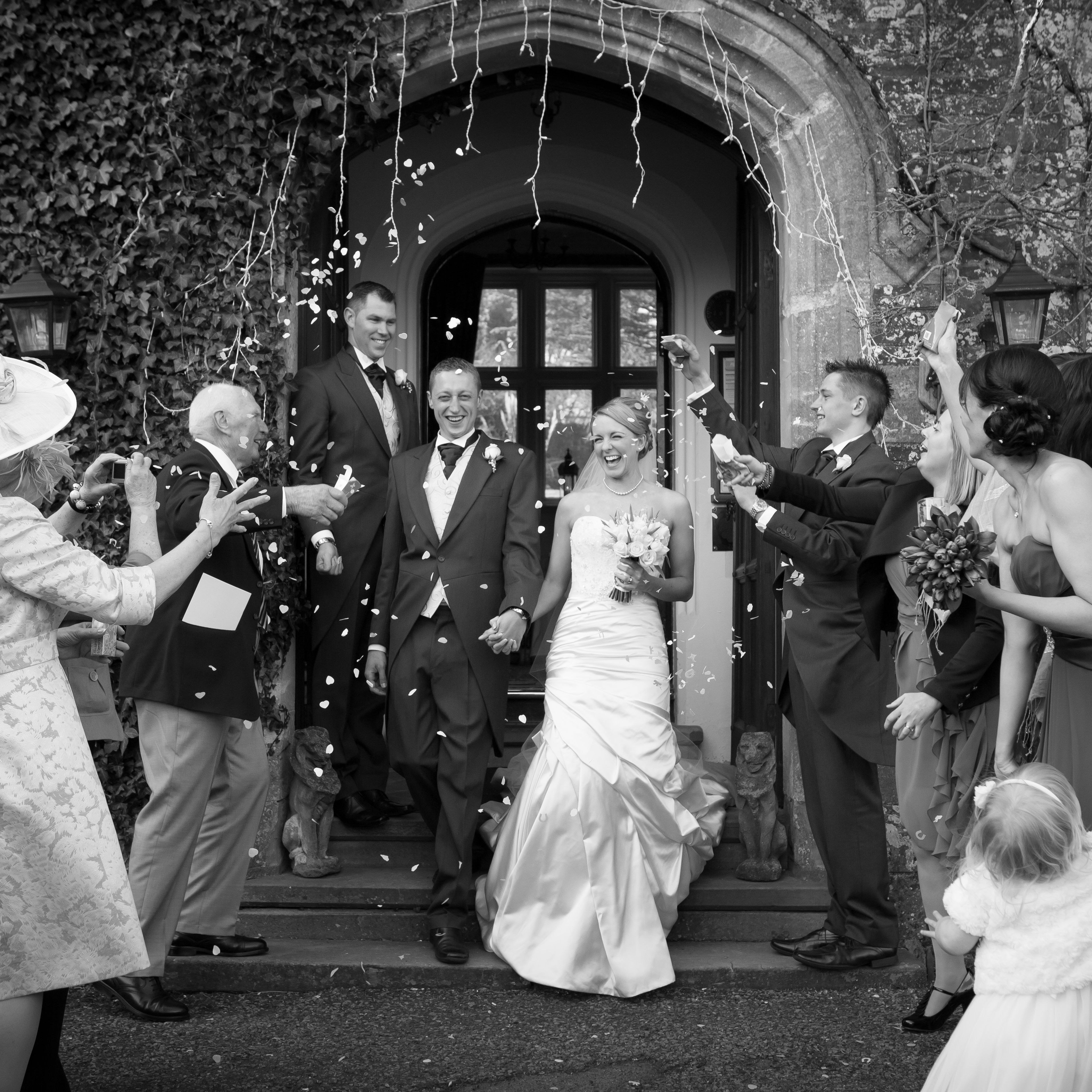Bride and groom exiting a building while guests throw confetti during a wedding celebration.