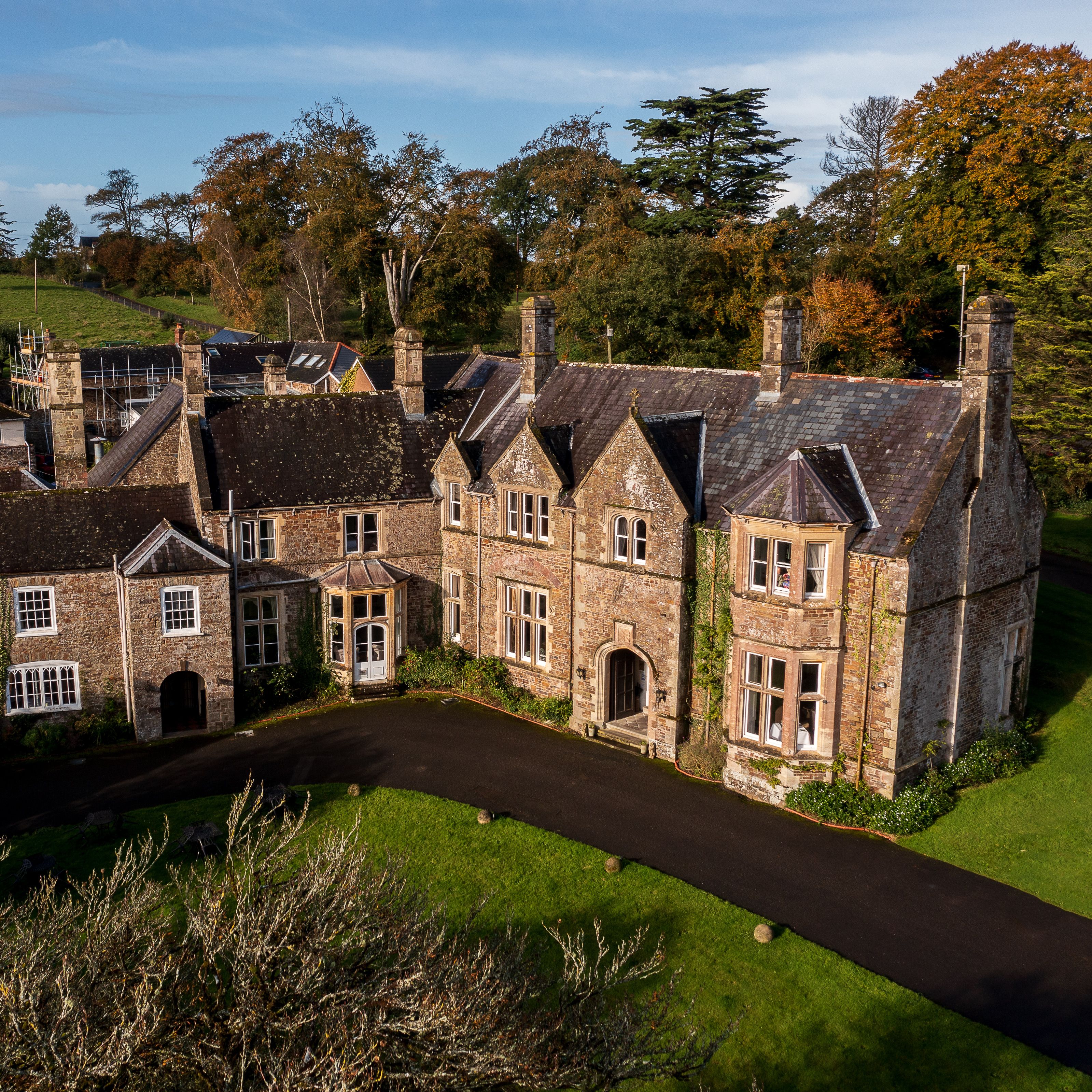 Aerial view of a large, historic stone manor house surrounded by gardens and countryside.
