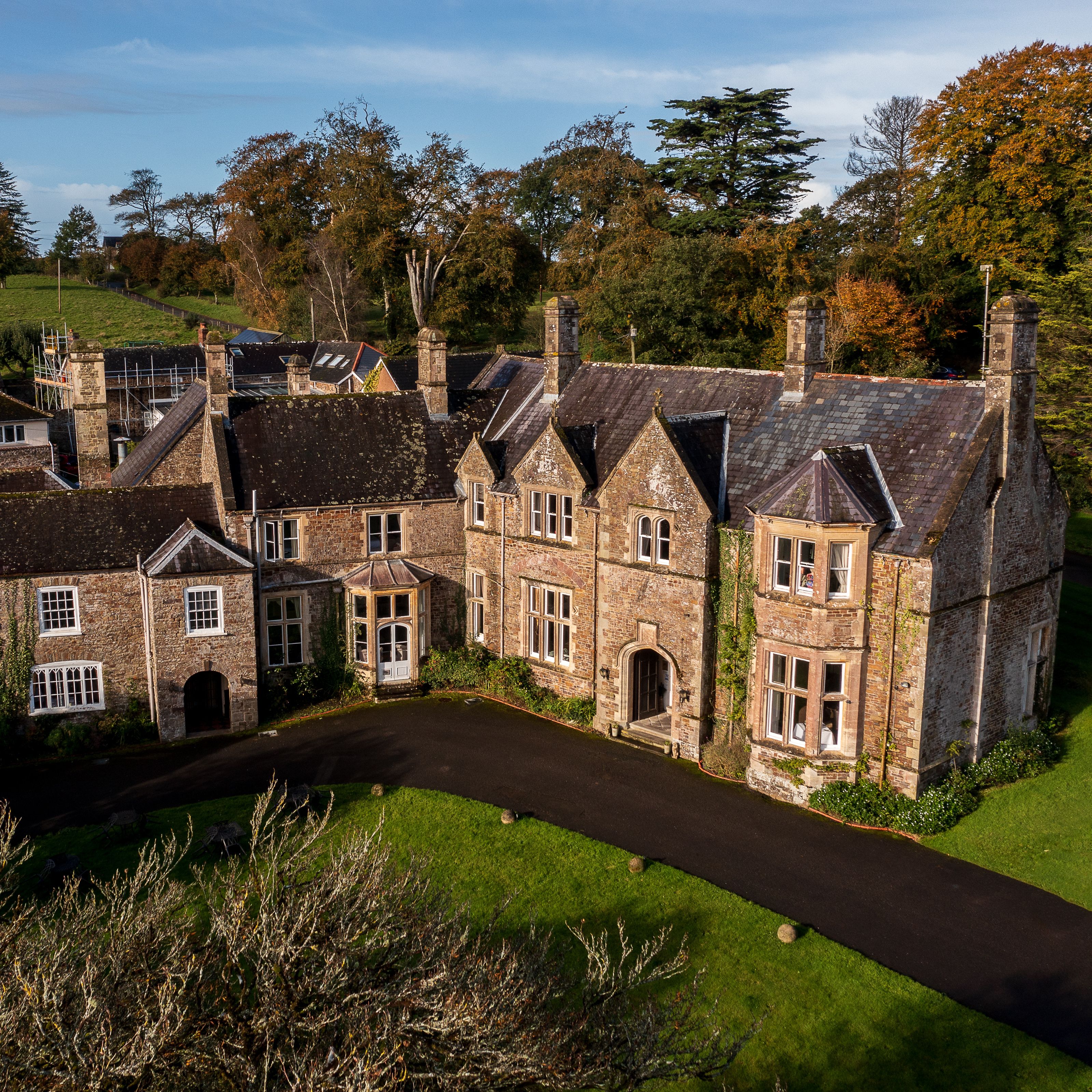 Aerial view of a large, historic stone manor house surrounded by gardens and countryside.