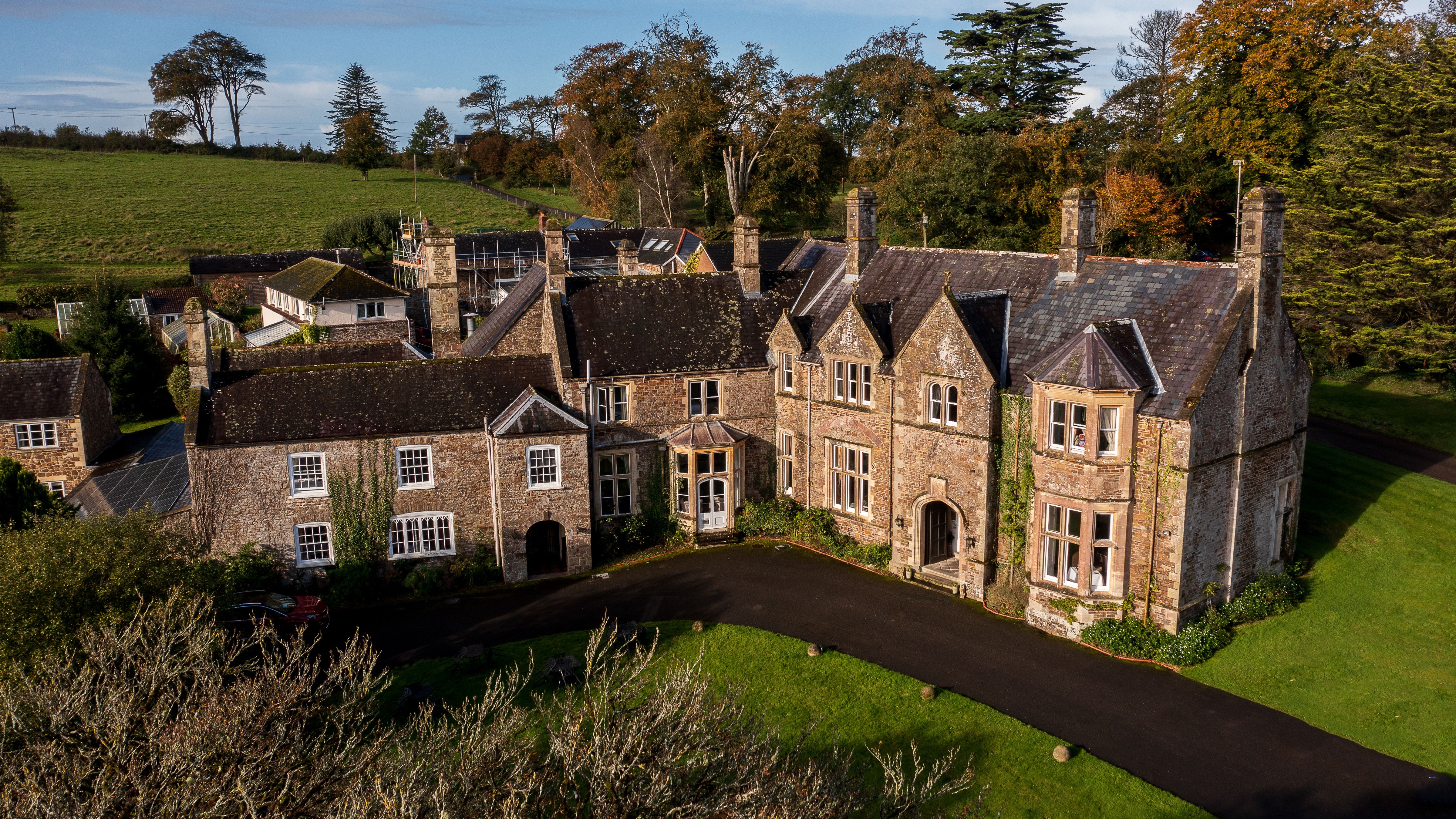 Aerial view of a large, historic stone manor house surrounded by gardens and countryside.