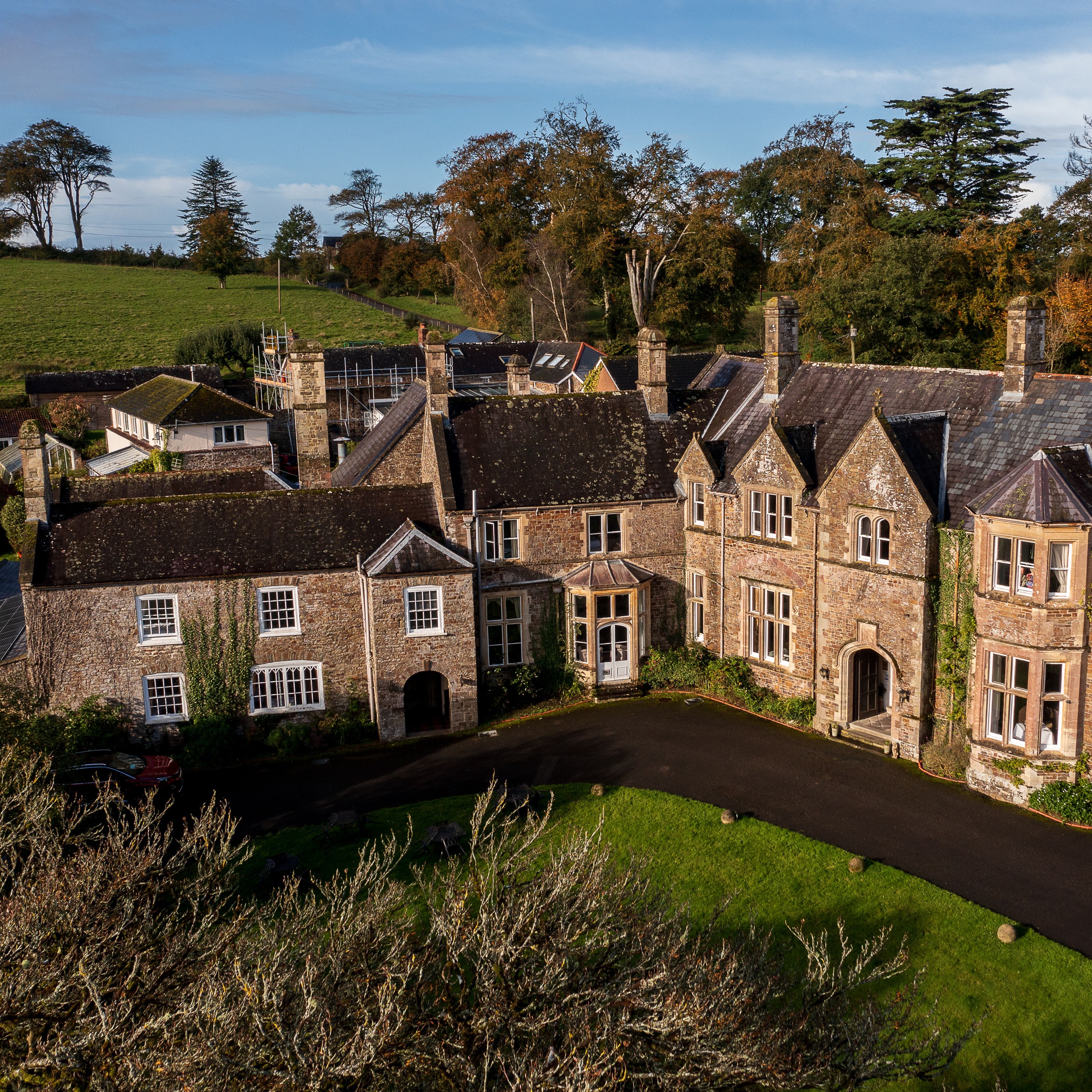 Aerial view of a large, historic stone manor house surrounded by gardens and countryside.