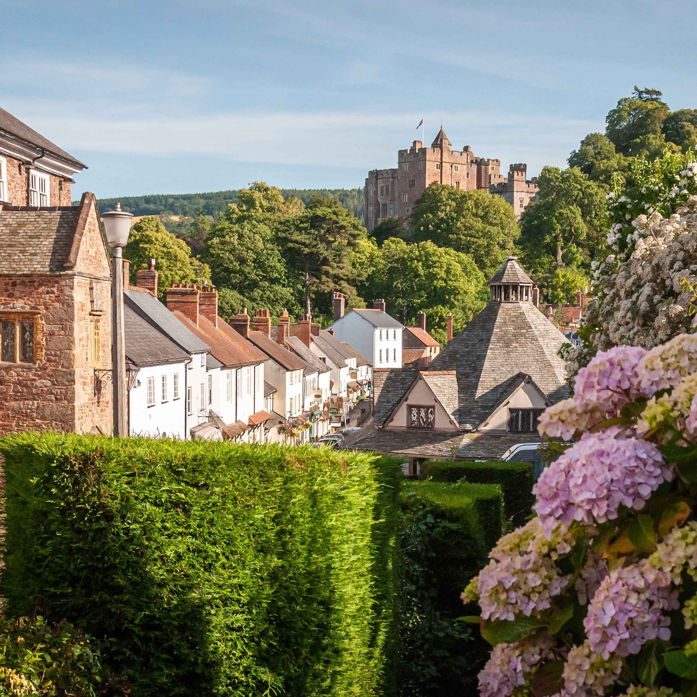 Picturesque English village with flowers, historic stone buildings, and a castle on a hill in the background