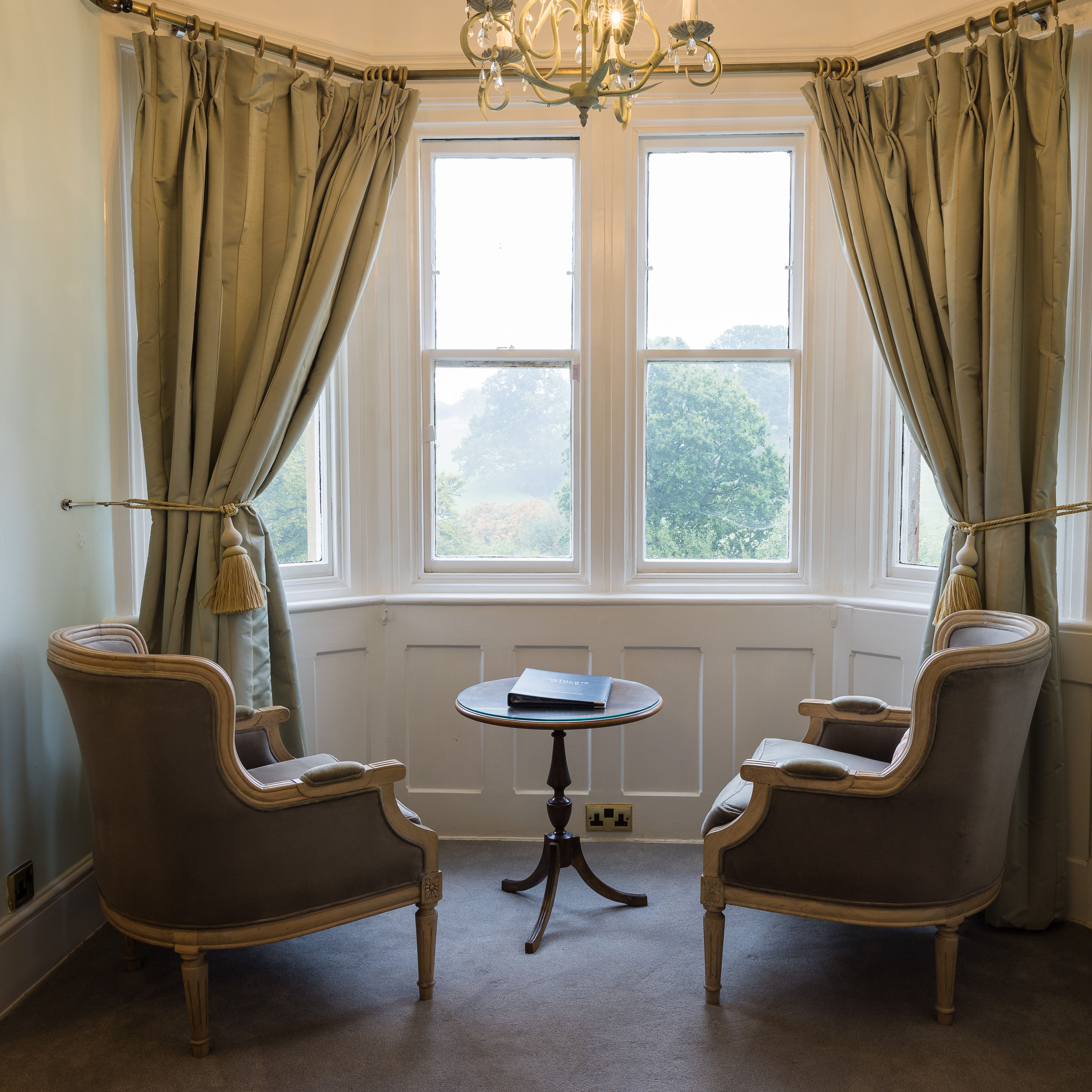 Elegant sitting area with two armchairs, a small round table, and large bay windows with curtains.