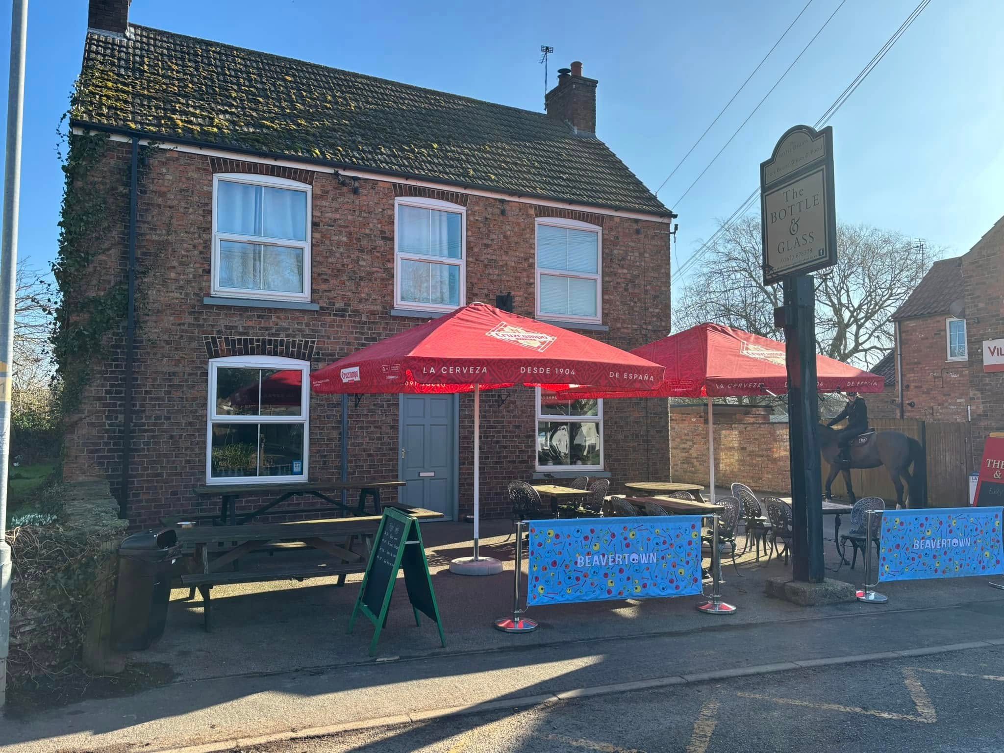 The front of The Bottle and Glass pub with red umbrellas and benches outside