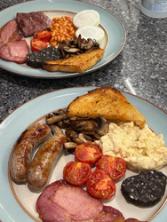 Two plates of full english breakfasts with eggs, sausages, black pudding, bacon,tomatoes, mushrooms and fried bread