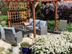 Patio in garden with chairs, sofa and table surrounded by flowers