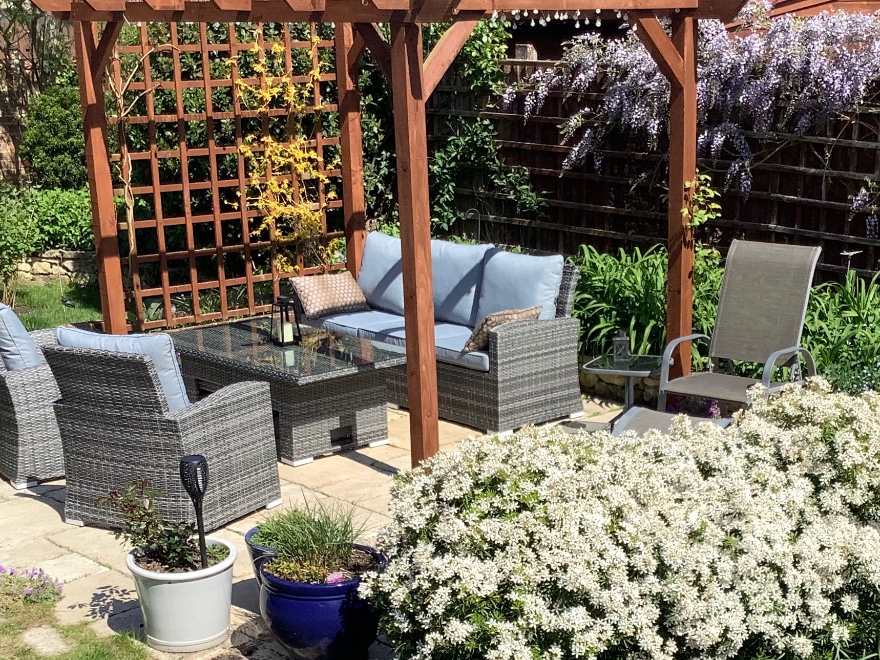 Patio in garden with chairs, sofa and table surrounded by flowers