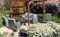 Patio in garden with chairs, sofa and table surrounded by flowers