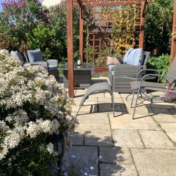 Patio in garden with chairs, sofa and table surrounded by flowers