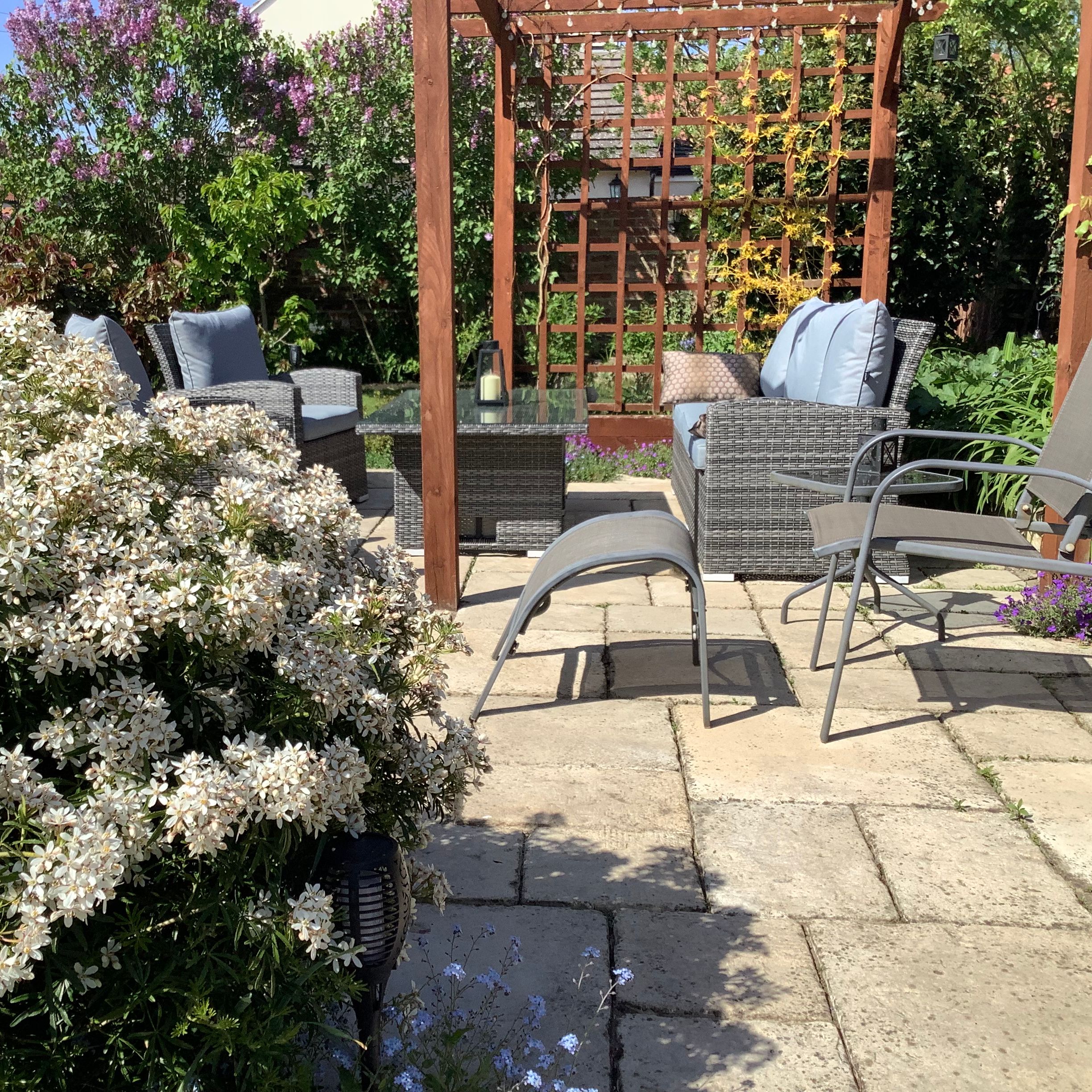 Patio in garden with chairs, sofa and table surrounded by flowers