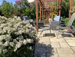 Patio in garden with chairs, sofa and table surrounded by flowers