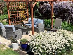 Patio in garden with chairs, sofa and table surrounded by flowers