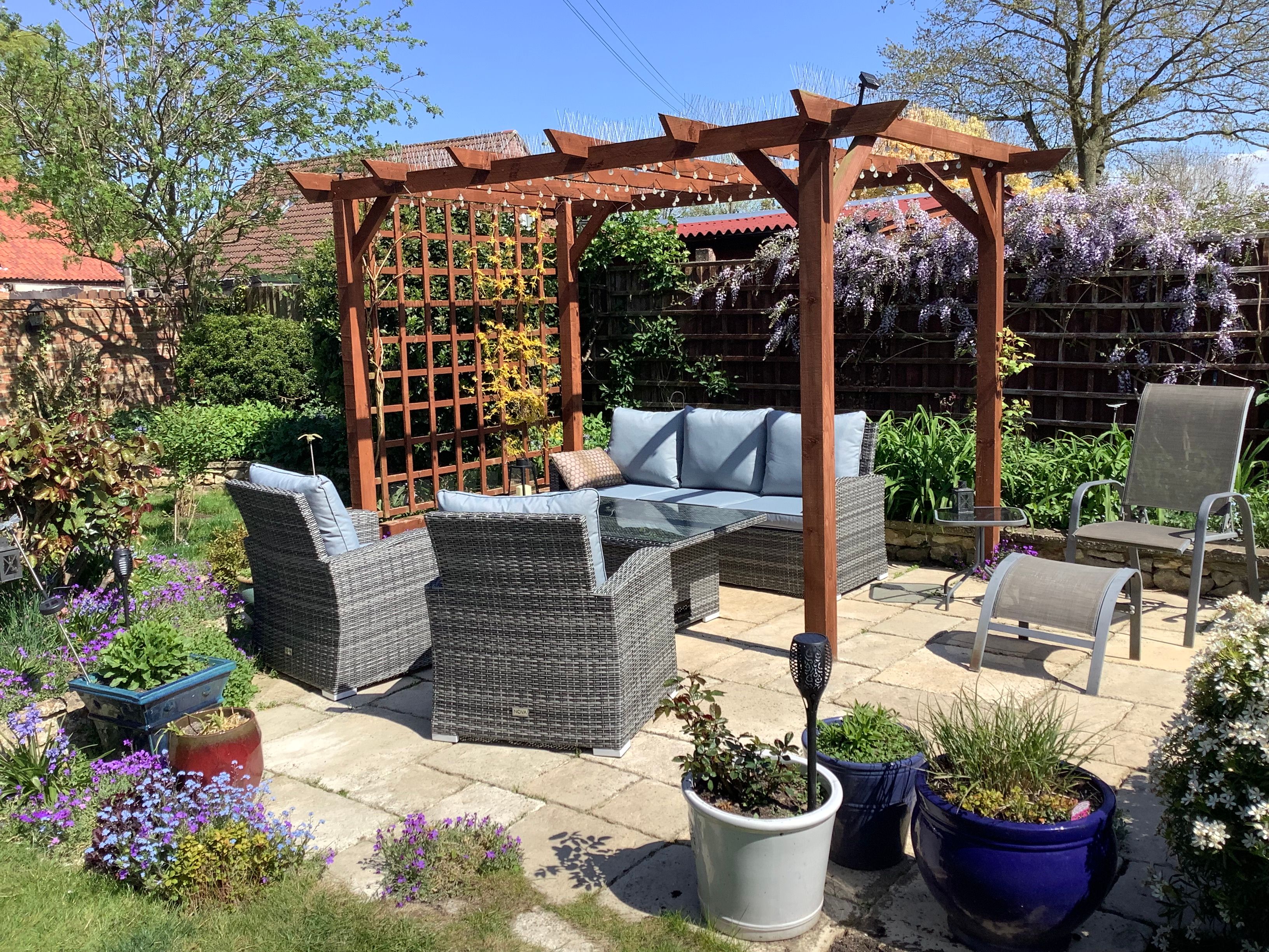 Patio in garden with chairs, sofa and table surrounded by flowers